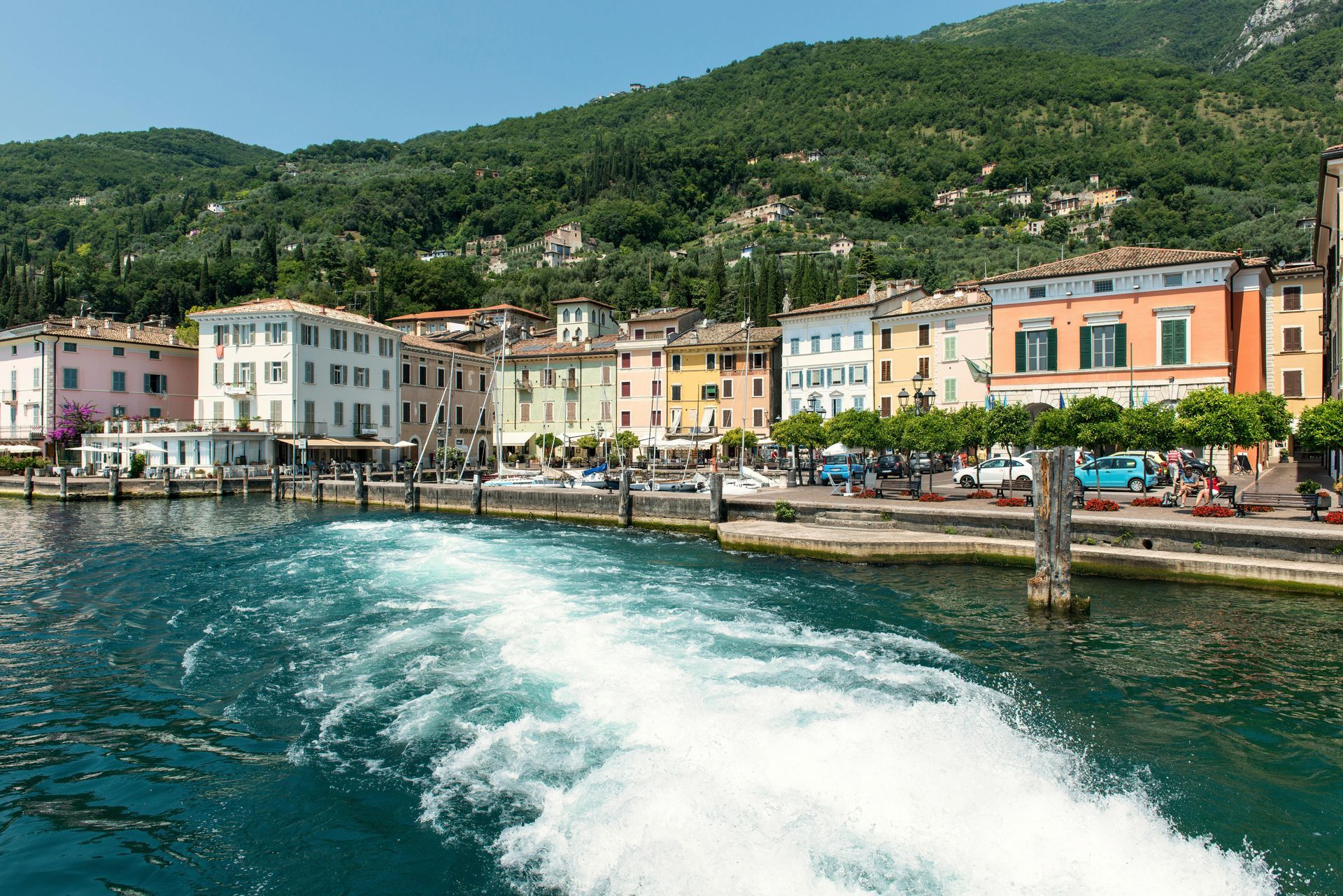 Colorful waterfront village with boats, harbor water, and green hills in the background
