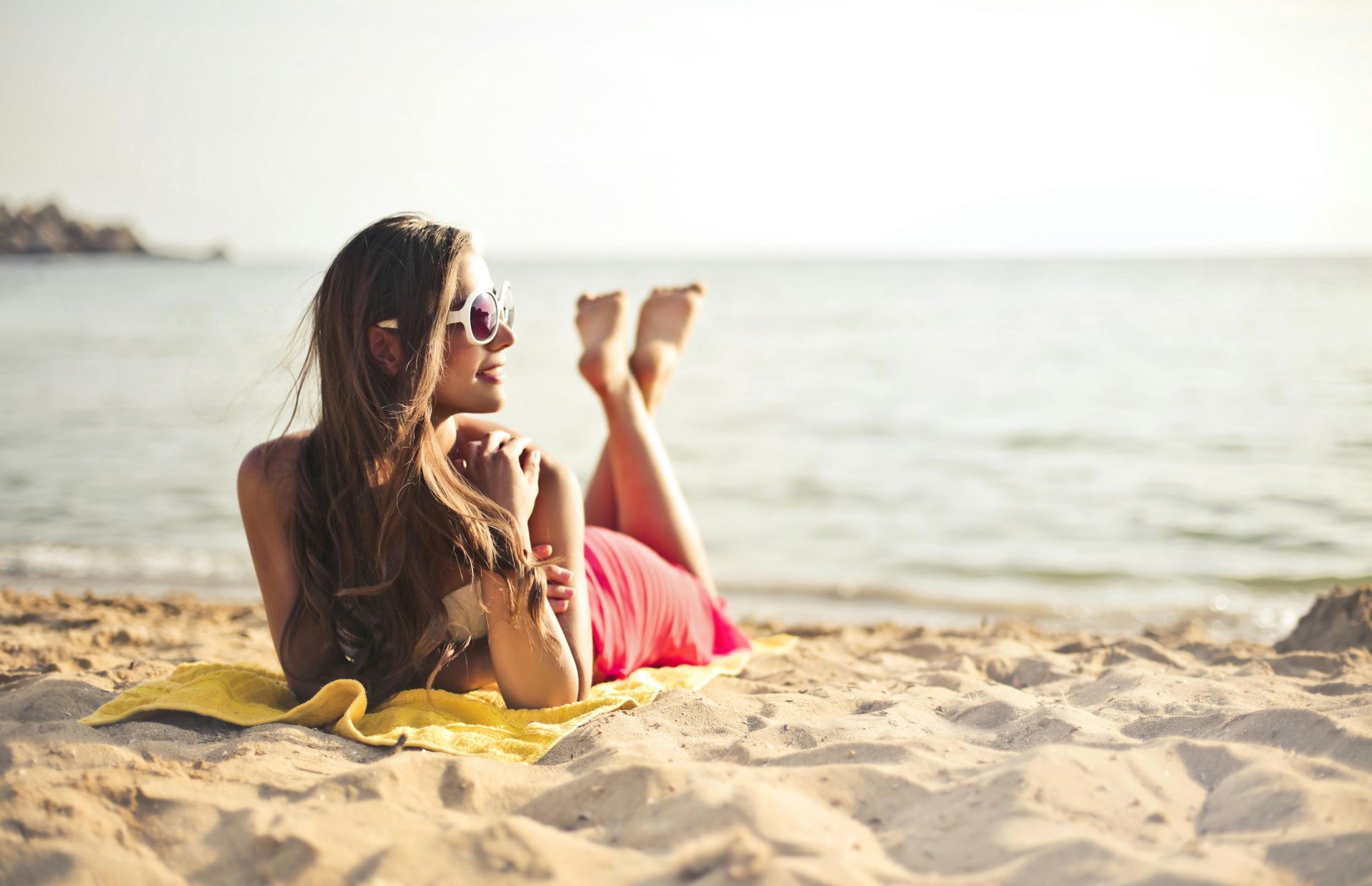 Person relaxing on a towel at the beach, looking out at the water at sunset.