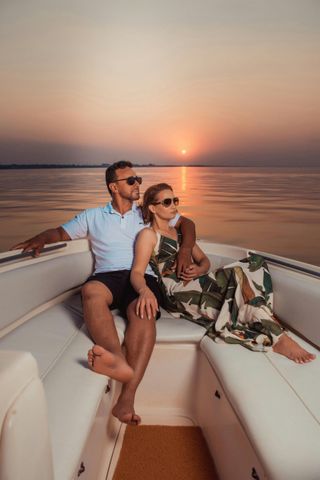 Couple relaxing on a boat at sunset, with calm water and a warm orange sky.