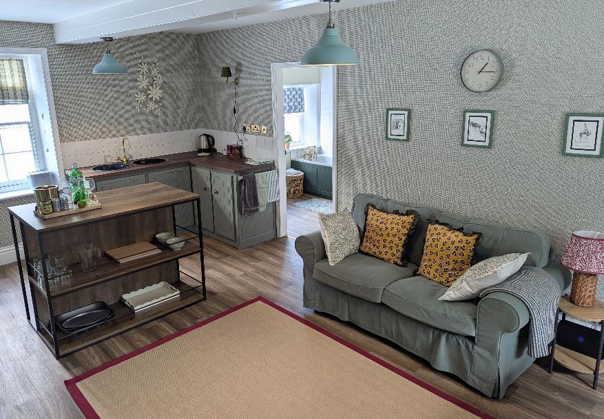 Cozy living space with open kitchen. Grey walls, teal accents, light-colored sofa, wooden island, and rug.