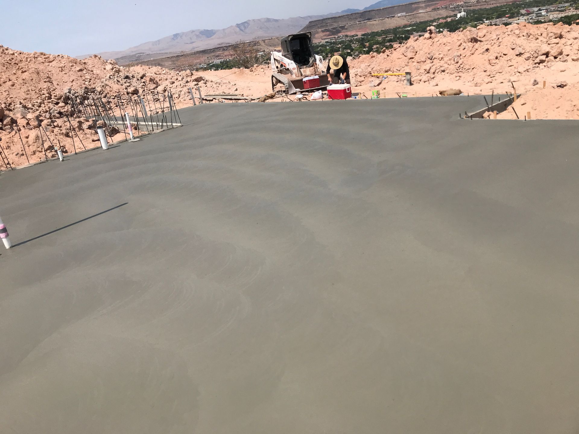 Fresh concrete slab being poured in a rocky desert landscape with workers and equipment in the distance