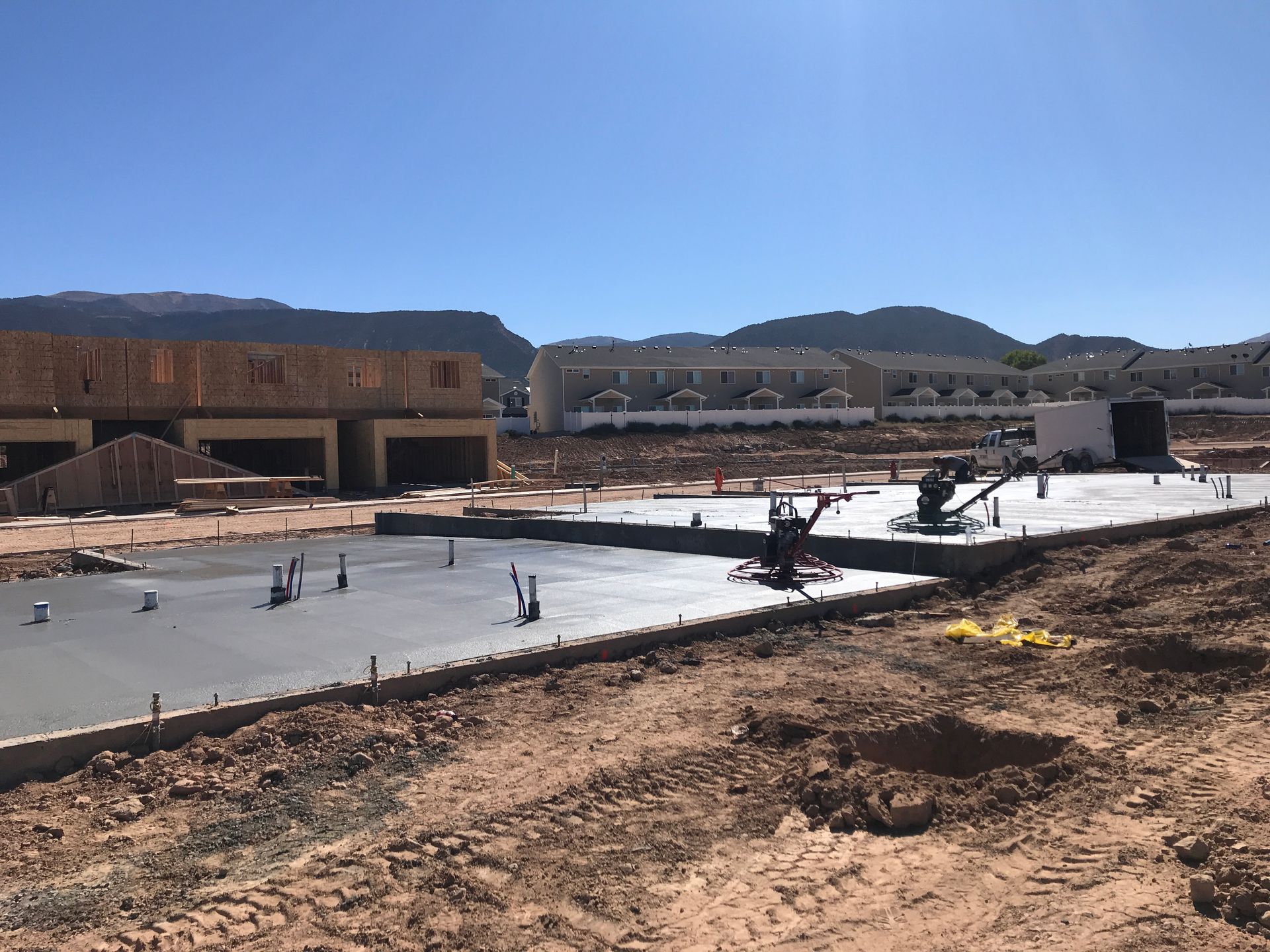 Construction site with concrete slab, workers in distance, and hills under a clear blue sky