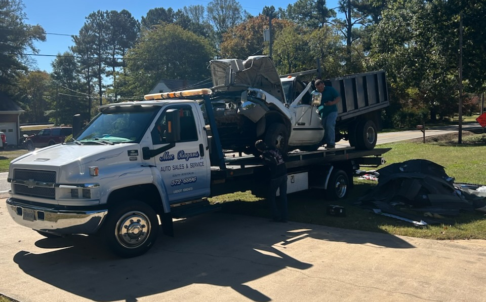 Tow truck loading a white truck bed with debris on a residential street; two people present | Chip Ragans Auto, LLC