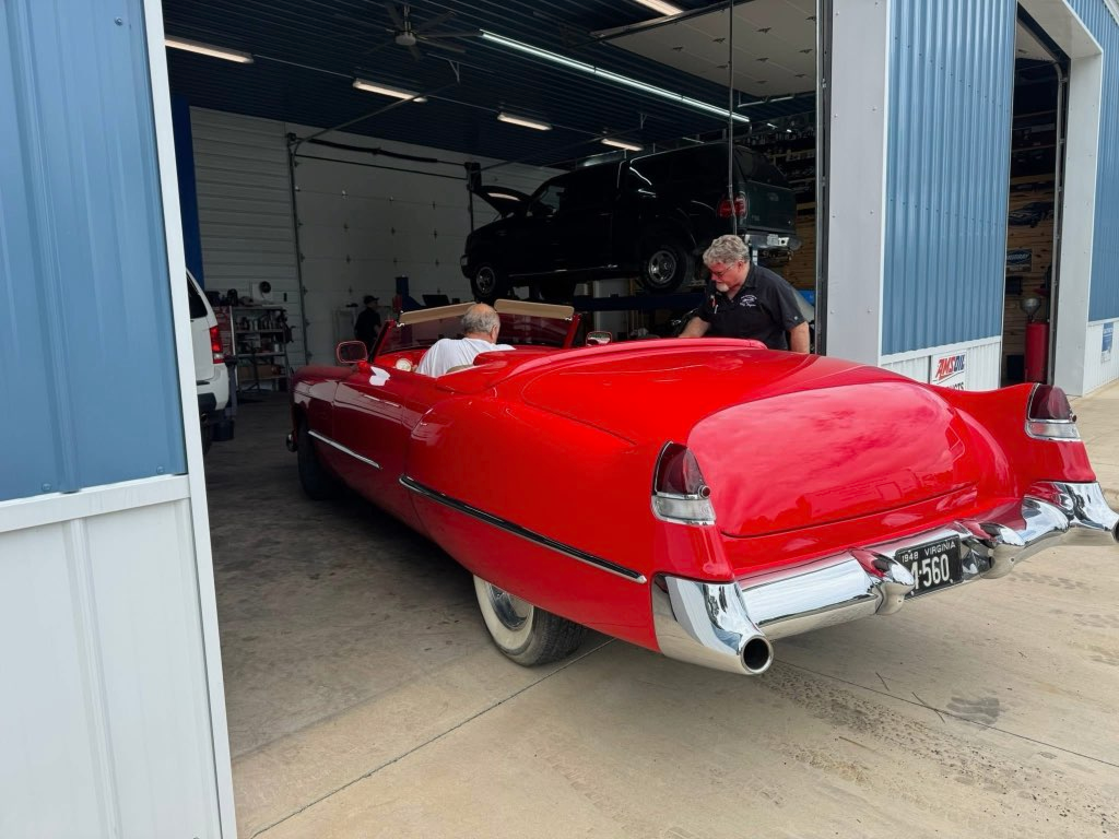Red classic convertible car exiting a garage; a man stands beside it | Chip Ragans Auto, LLC