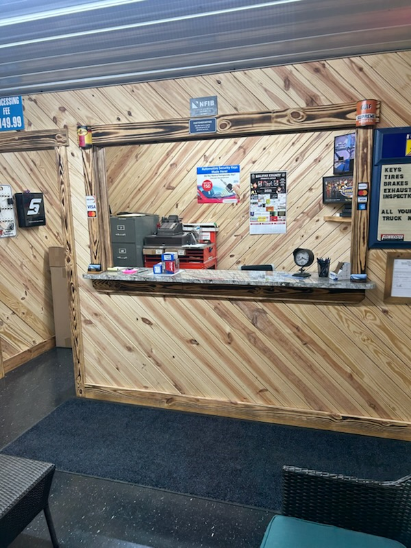 A counter inside a wood-paneled building with various items, including a cash register, signage, and a black mat on the floor | Chip Ragans Auto, LLC
