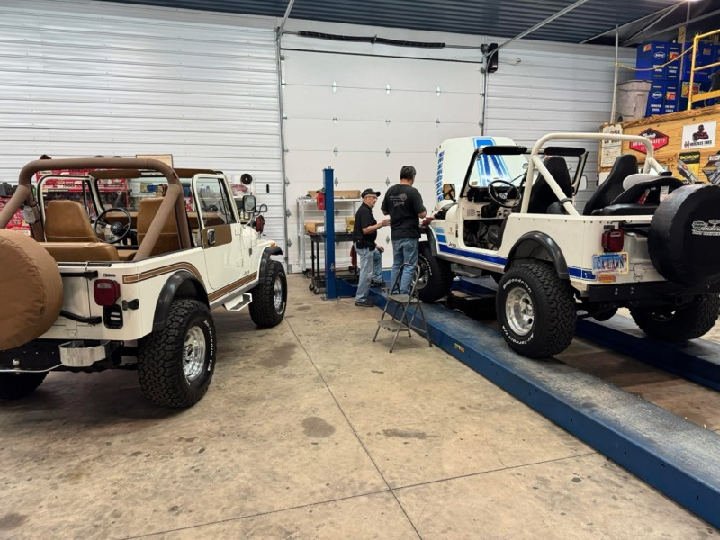 Two white Jeep CJ-7s inside a garage, with people working on the vehicles | Chip Ragans Auto, LLC