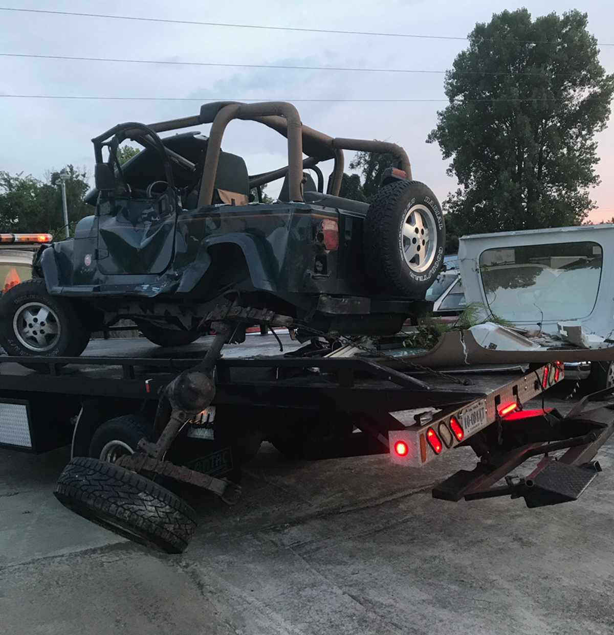 A severely damaged green Jeep Wrangler is being towed on a flatbed tow truck | Chip Ragans Auto, LLC