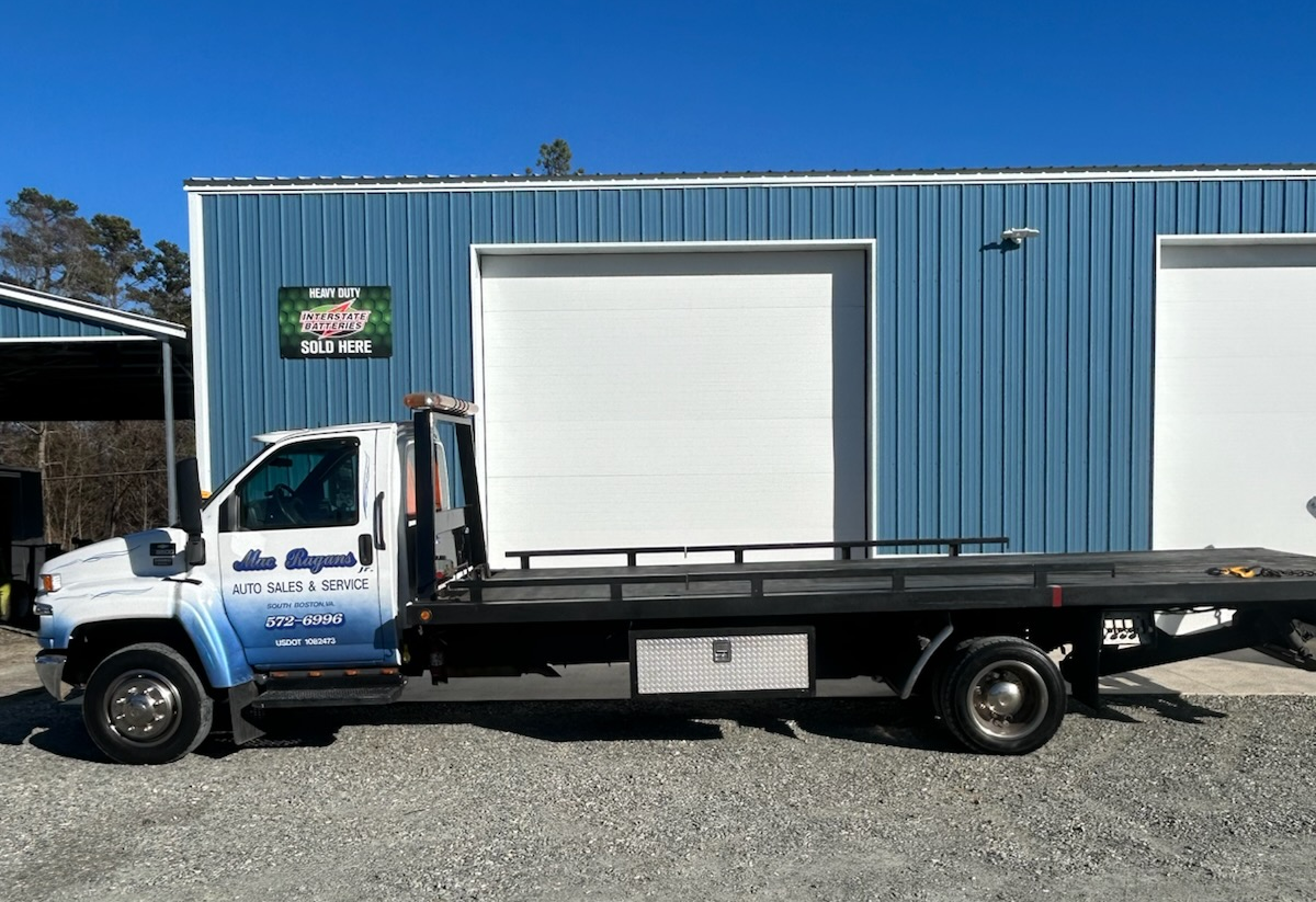 Tow truck parked in front of a blue building with white garage doors, sunny day | Chip Ragans Auto, LLC
