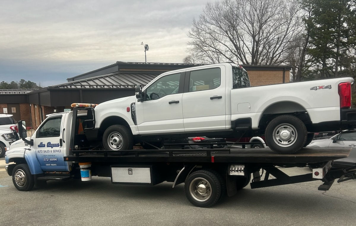 White tow truck transporting a white pickup truck on a flatbed. Cloudy outdoor setting | Chip Ragans Auto, LLC