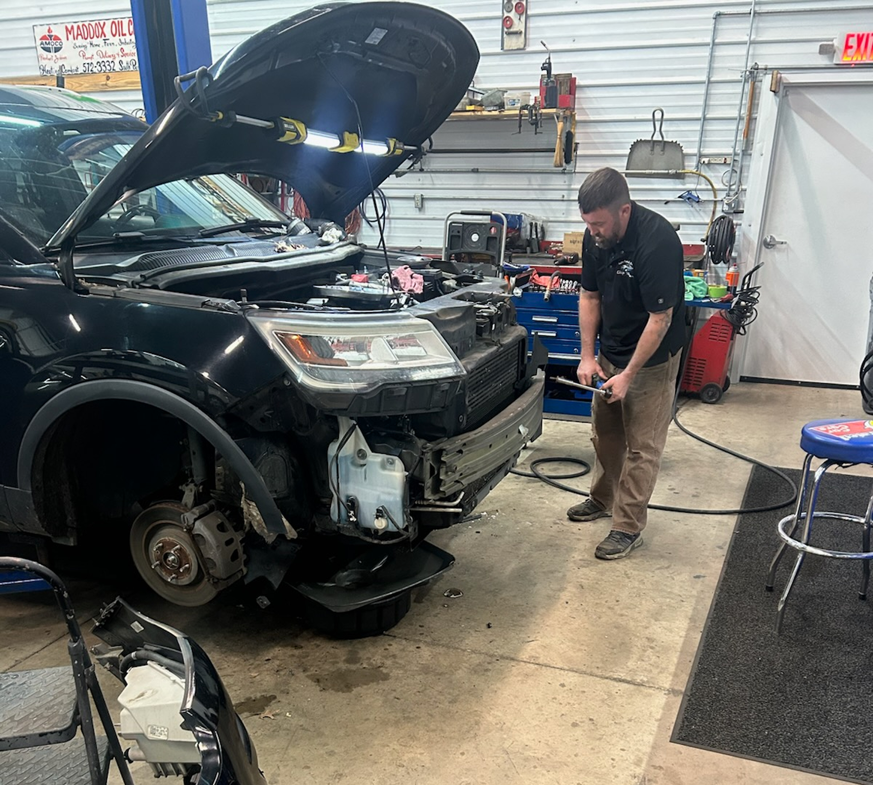 Mechanic working on a black car in a garage. Car's front bumper is off. The mechanic is using a wrench | Chip Ragans Auto, LLC