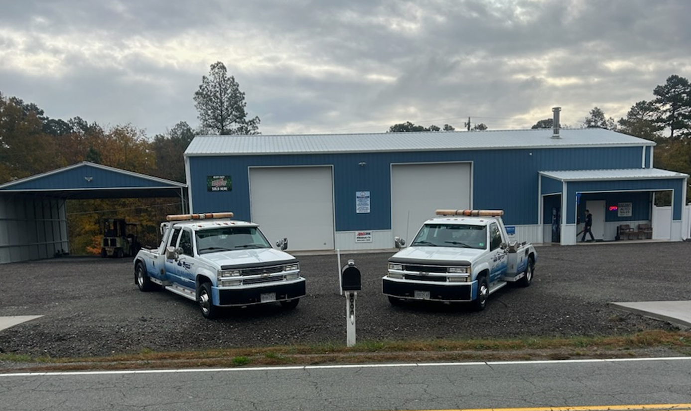 Two tow trucks parked in front of a blue building with white garage doors; overcast day | Chip Ragans Auto, LLC