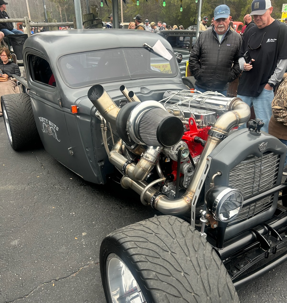 Gray hot rod with large turbo engine on display; two men observe | Chip Ragans Auto, LLC