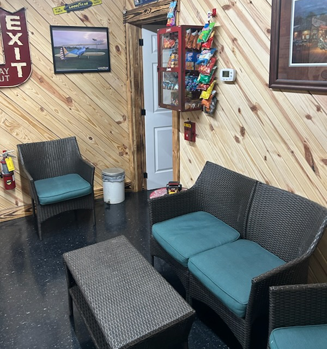 Waiting area with wicker furniture, wood paneling, snack rack, and exit sign | Chip Ragans Auto, LLC