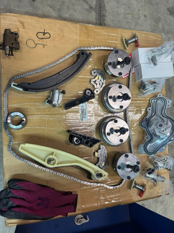 Engine timing chain components laid out on a wooden surface, including sprockets, chain, and tensioners | Chip Ragans Auto, LLC