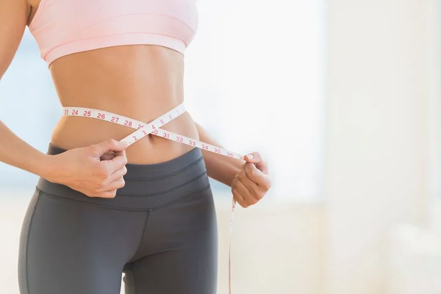 Woman in workout clothes measuring waist with a tape measure.