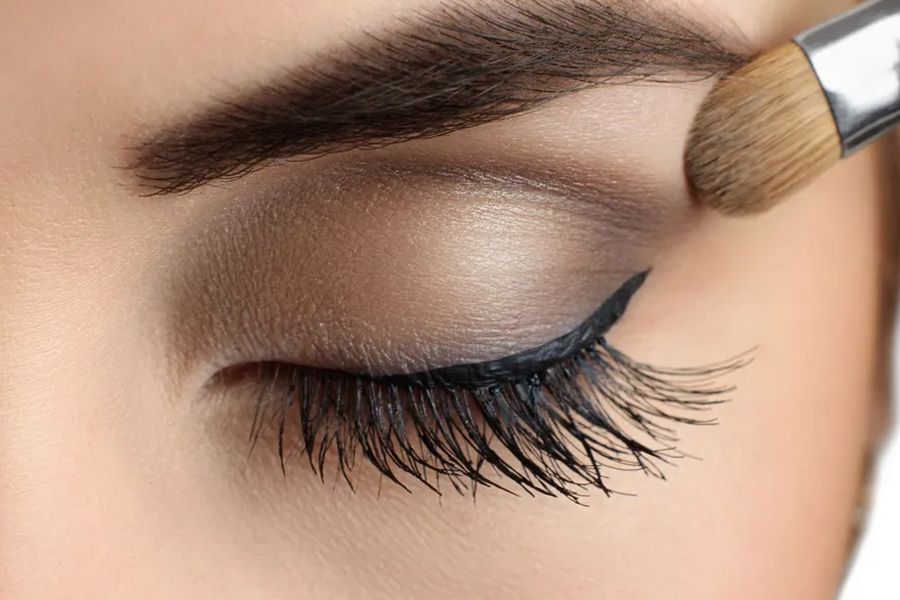 Eye with eyeshadow and makeup brush applying color. Dark eyeliner and long eyelashes.
