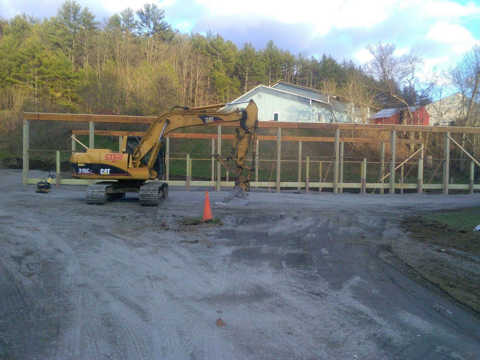 A yellow excavator is parked in a dirt lot next to an orange cone.