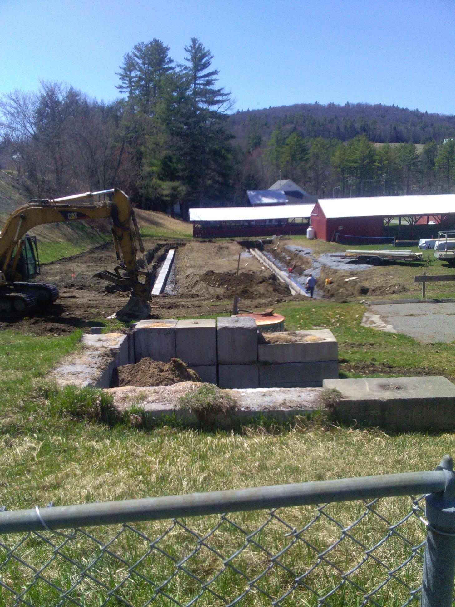 An excavator is digging a hole in a field with a barn in the background