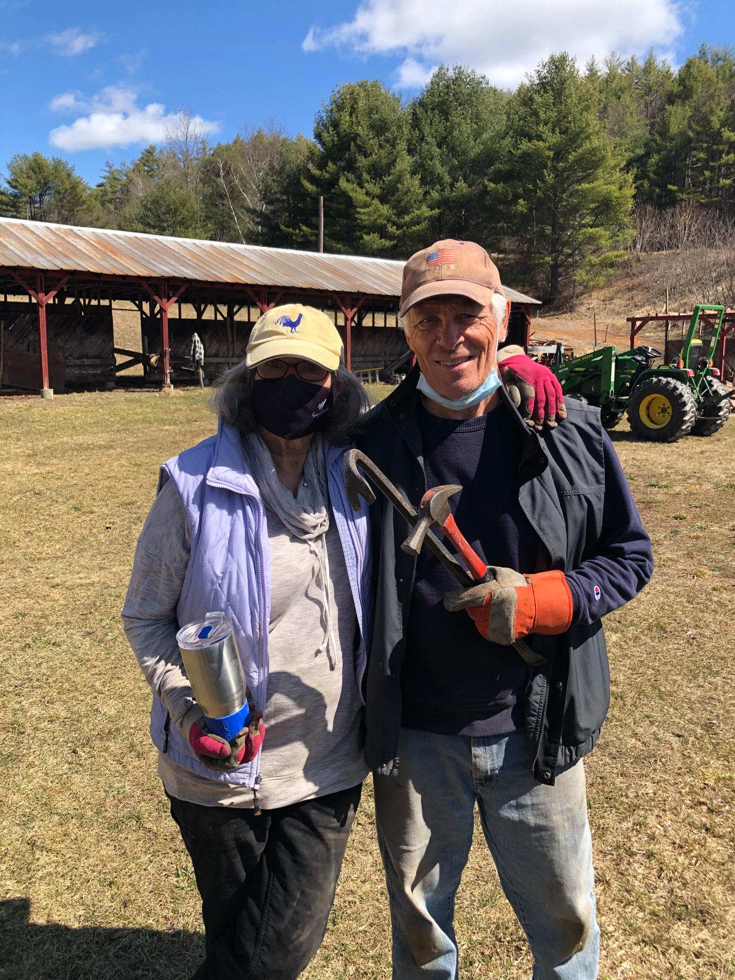 A man and a woman are standing next to each other in a field holding tools.
