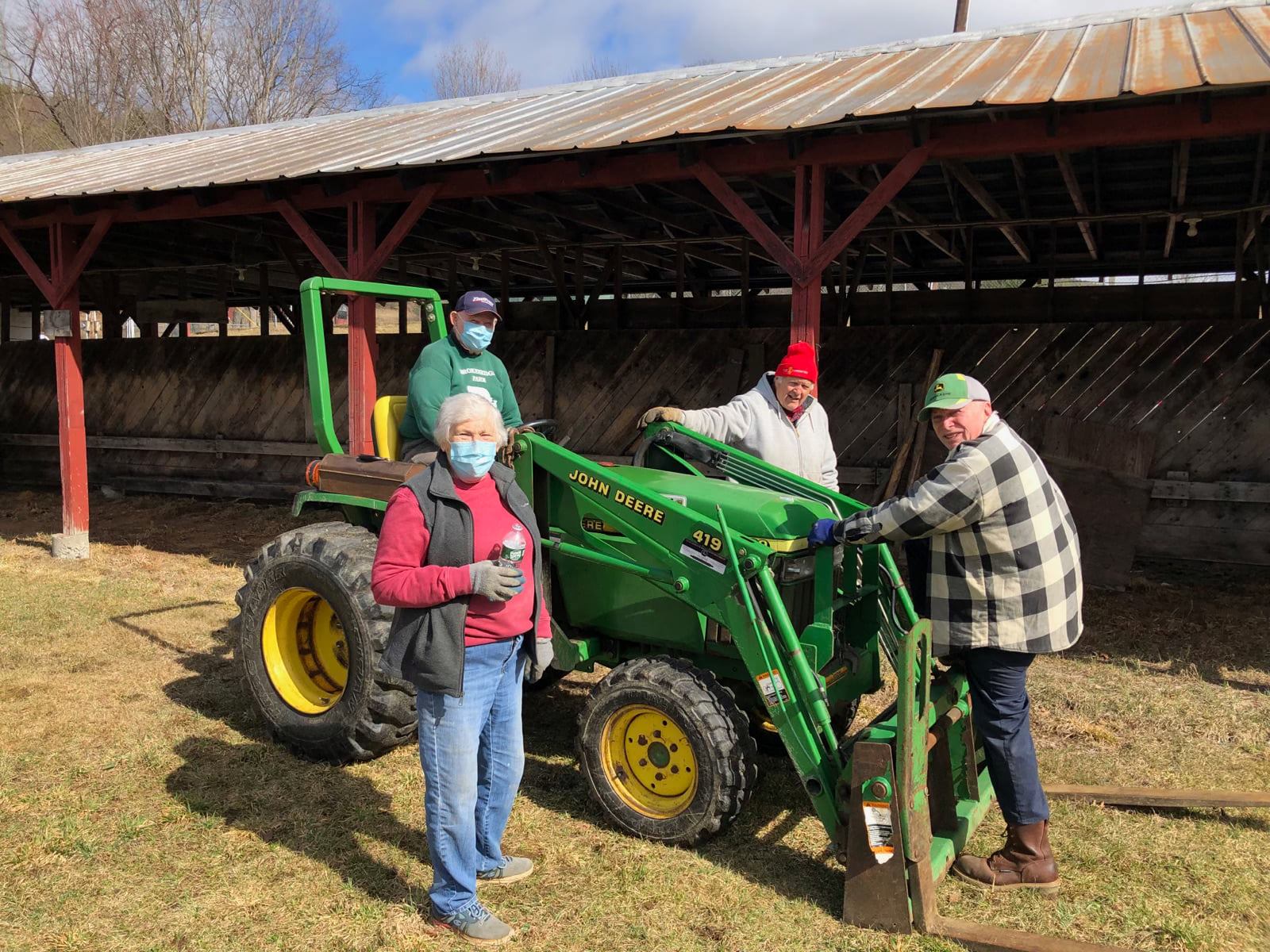 A group of people are standing next to a green john deere tractor.