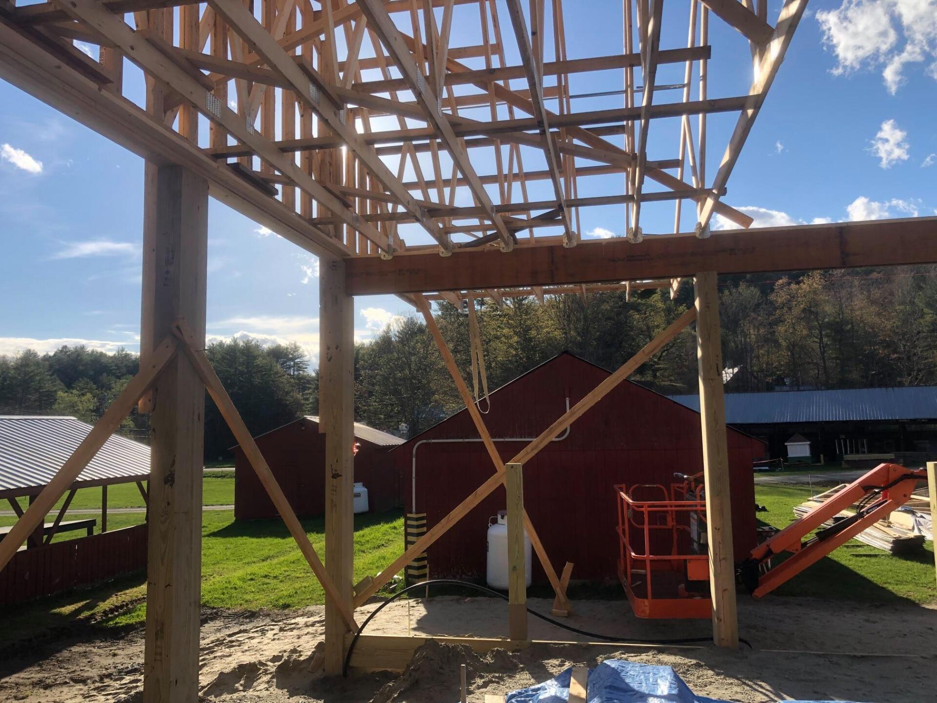 A large wooden structure is being built with a red barn in the background