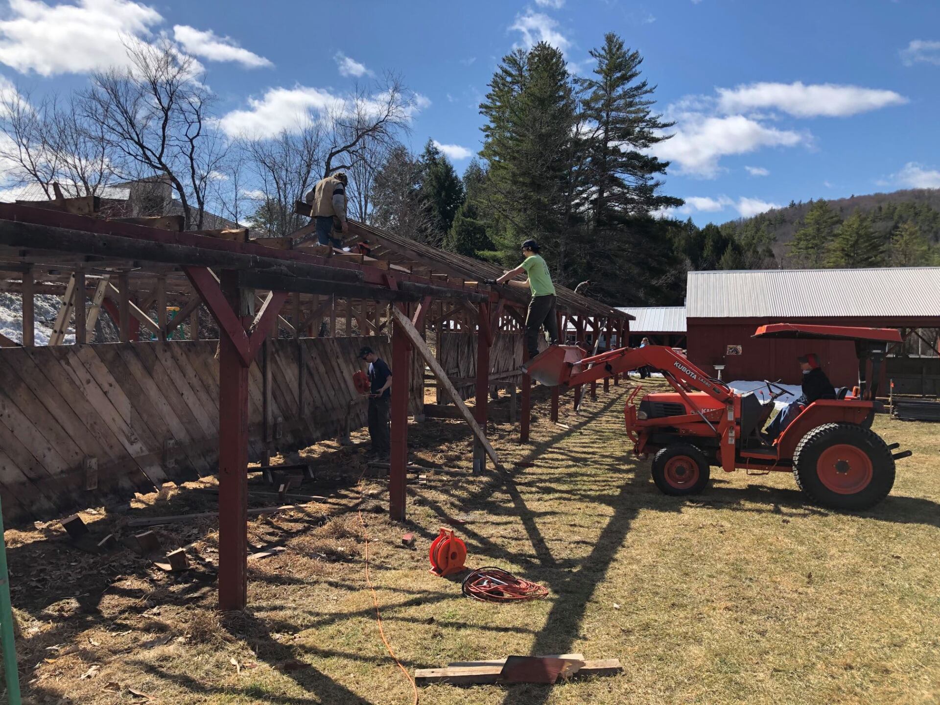 A tractor is parked in a field next to a wooden structure being built.