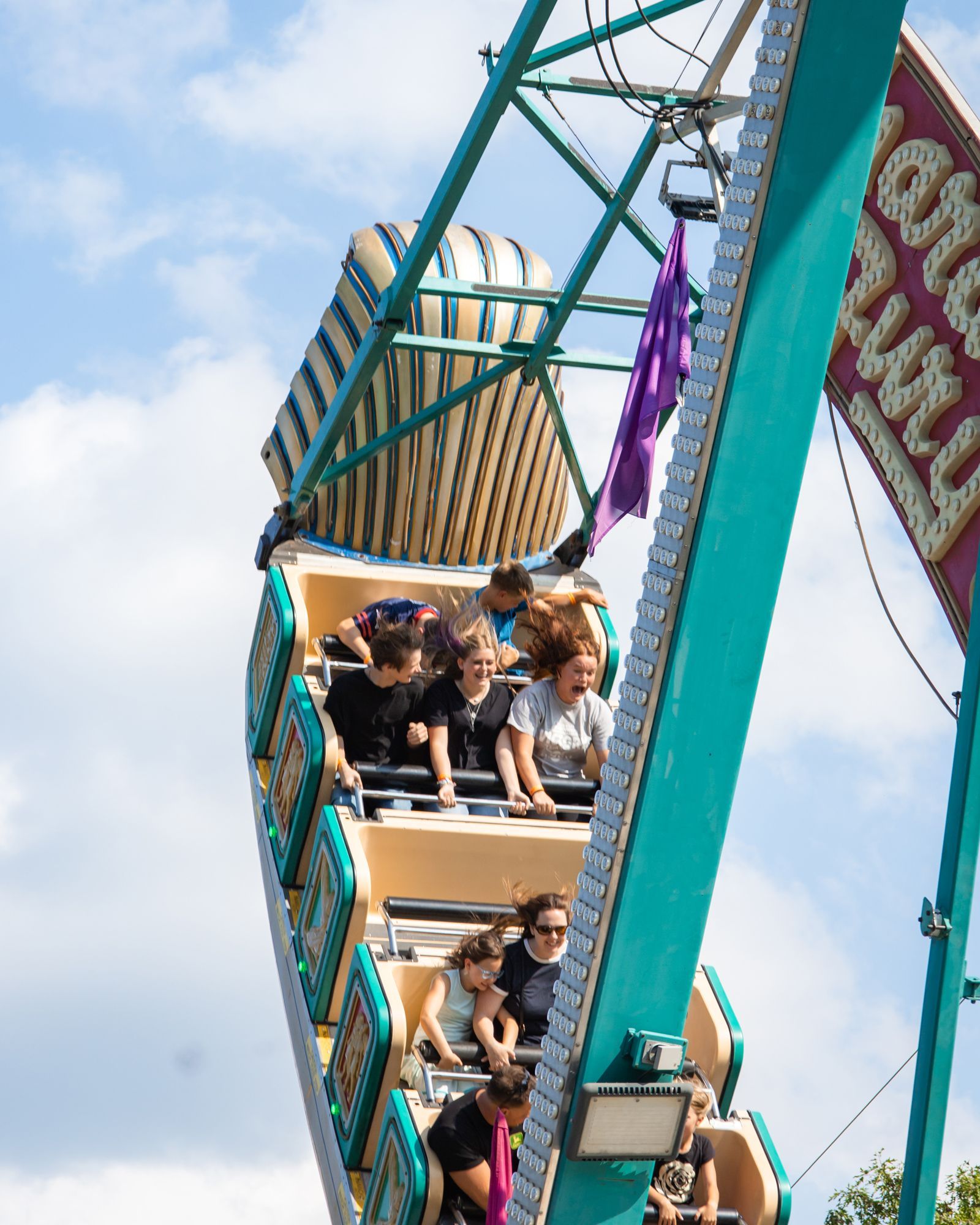 Riders in a teal-and-cream carnival ride spin against a cloudy sky