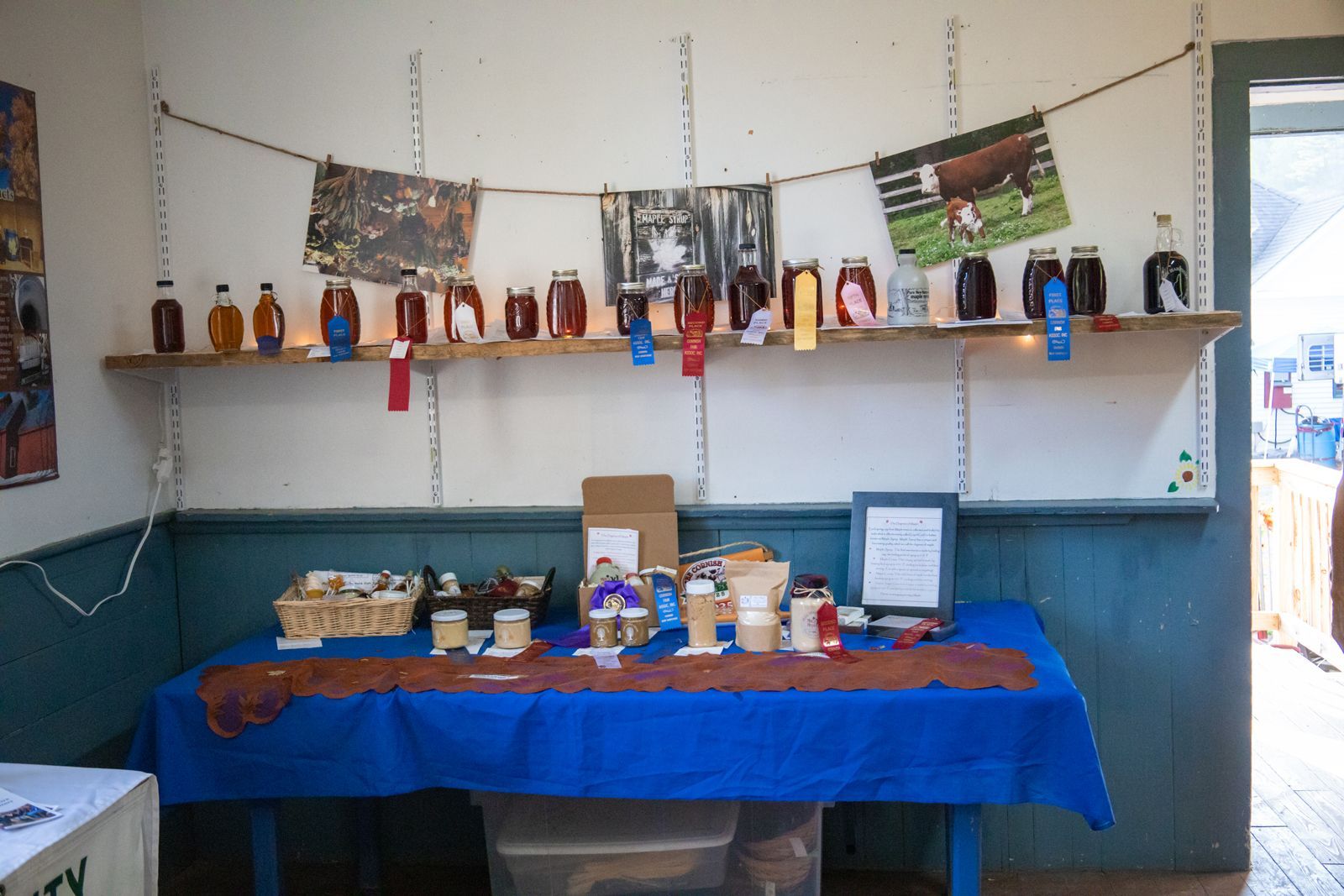 Small display table with bottles, jars, and handmade items on a blue cloth in a simple room
