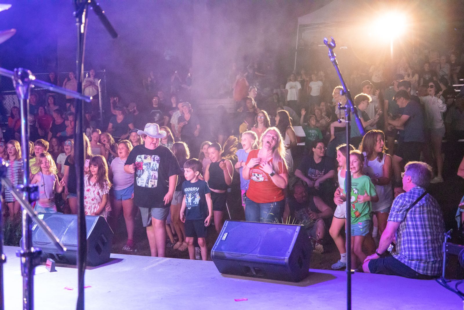 Crowd watching a live outdoor stage performance at night under bright lights