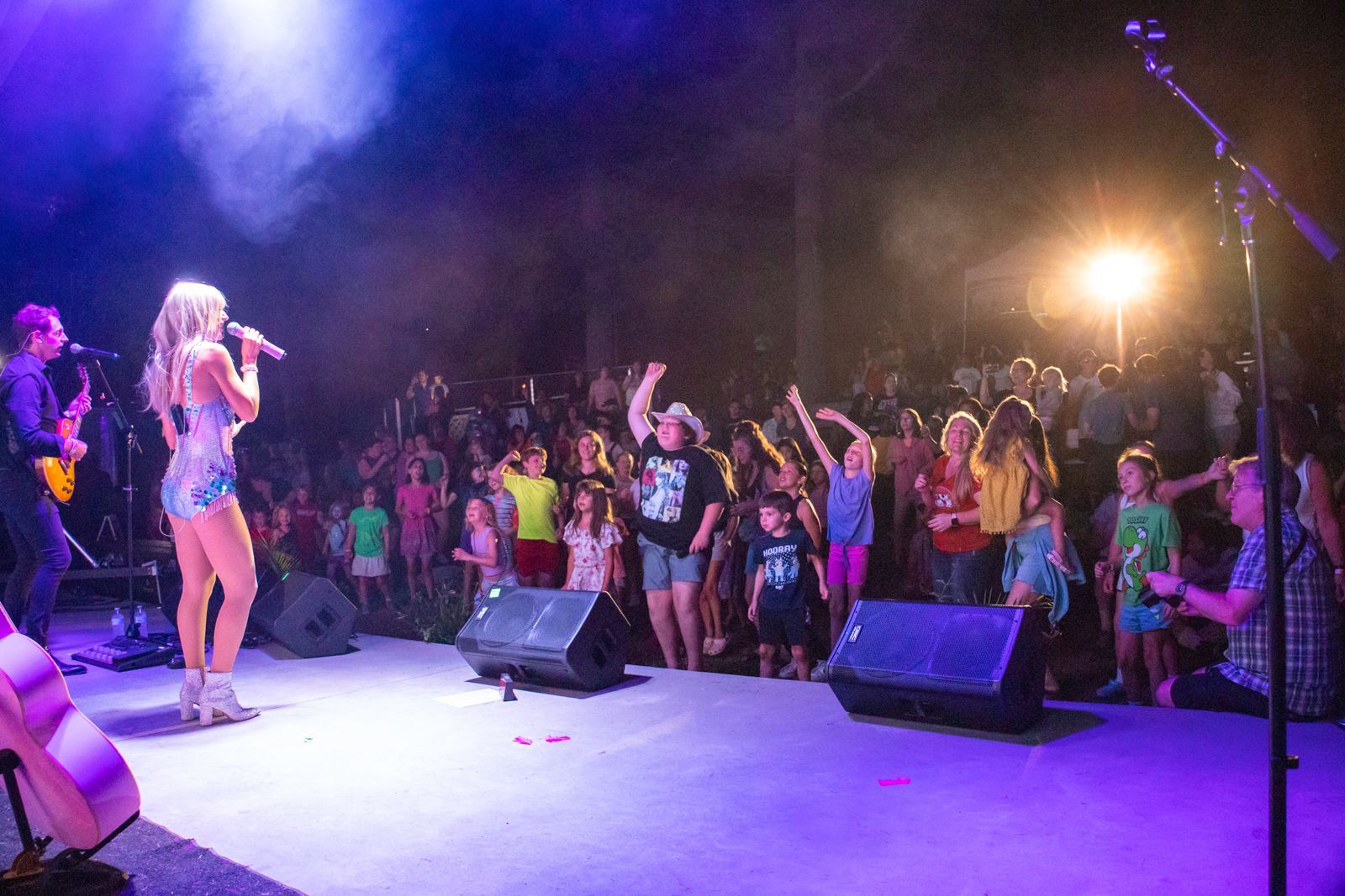 Singer performing on stage to a cheering crowd at a colorful nighttime concert