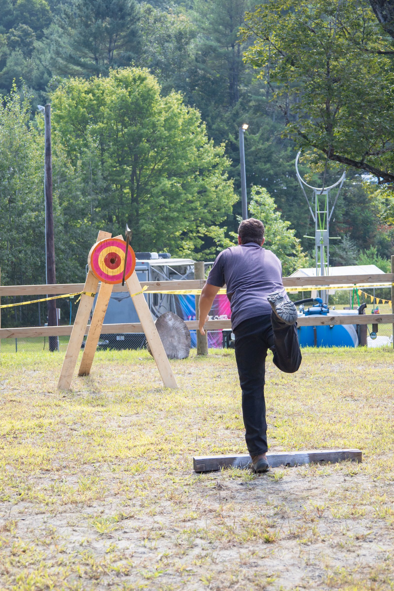 Person throws a hatchet at a target in an outdoor wooded area.