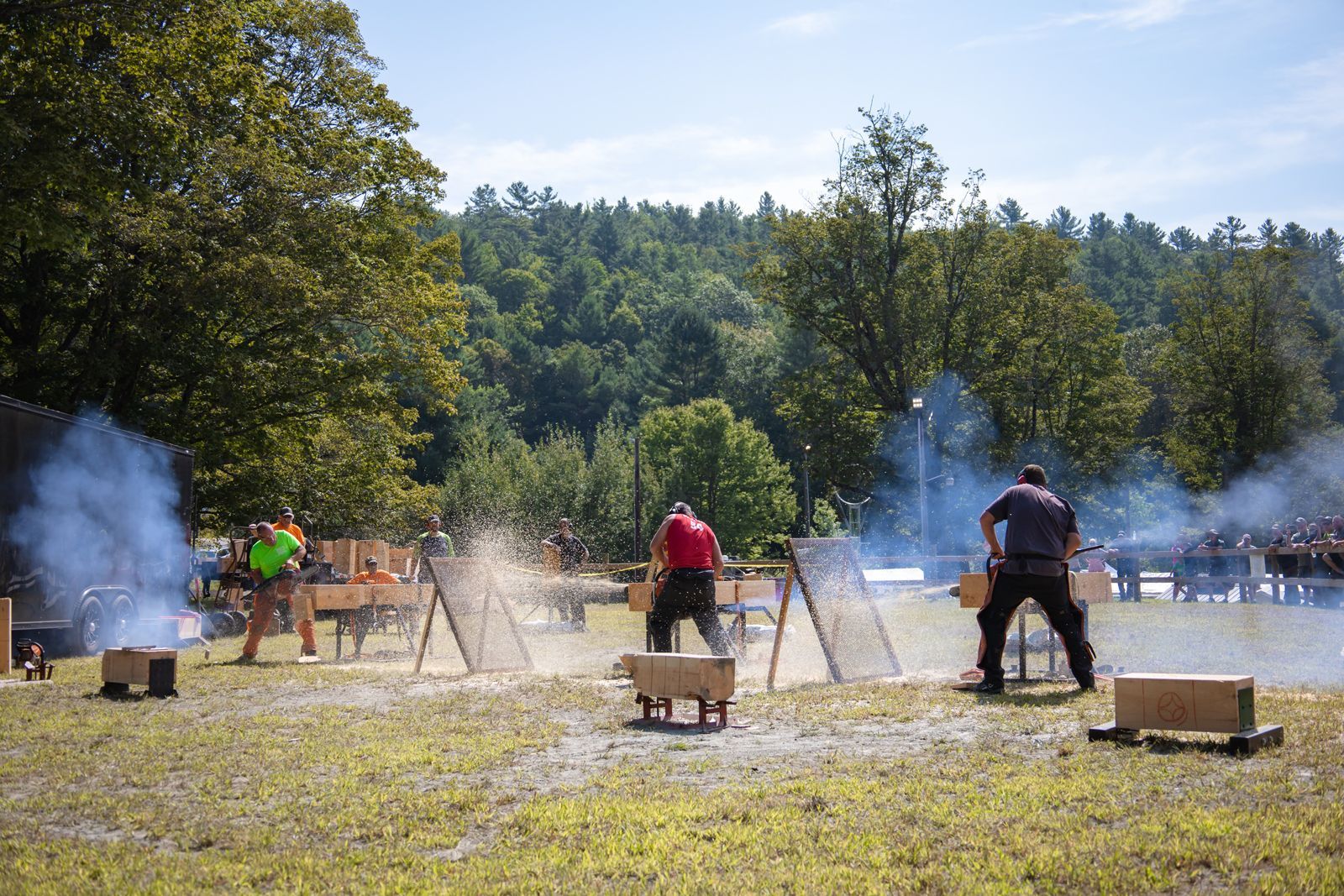 People outdoors at a smoky shooting range with targets and wooden stands in a wooded field
