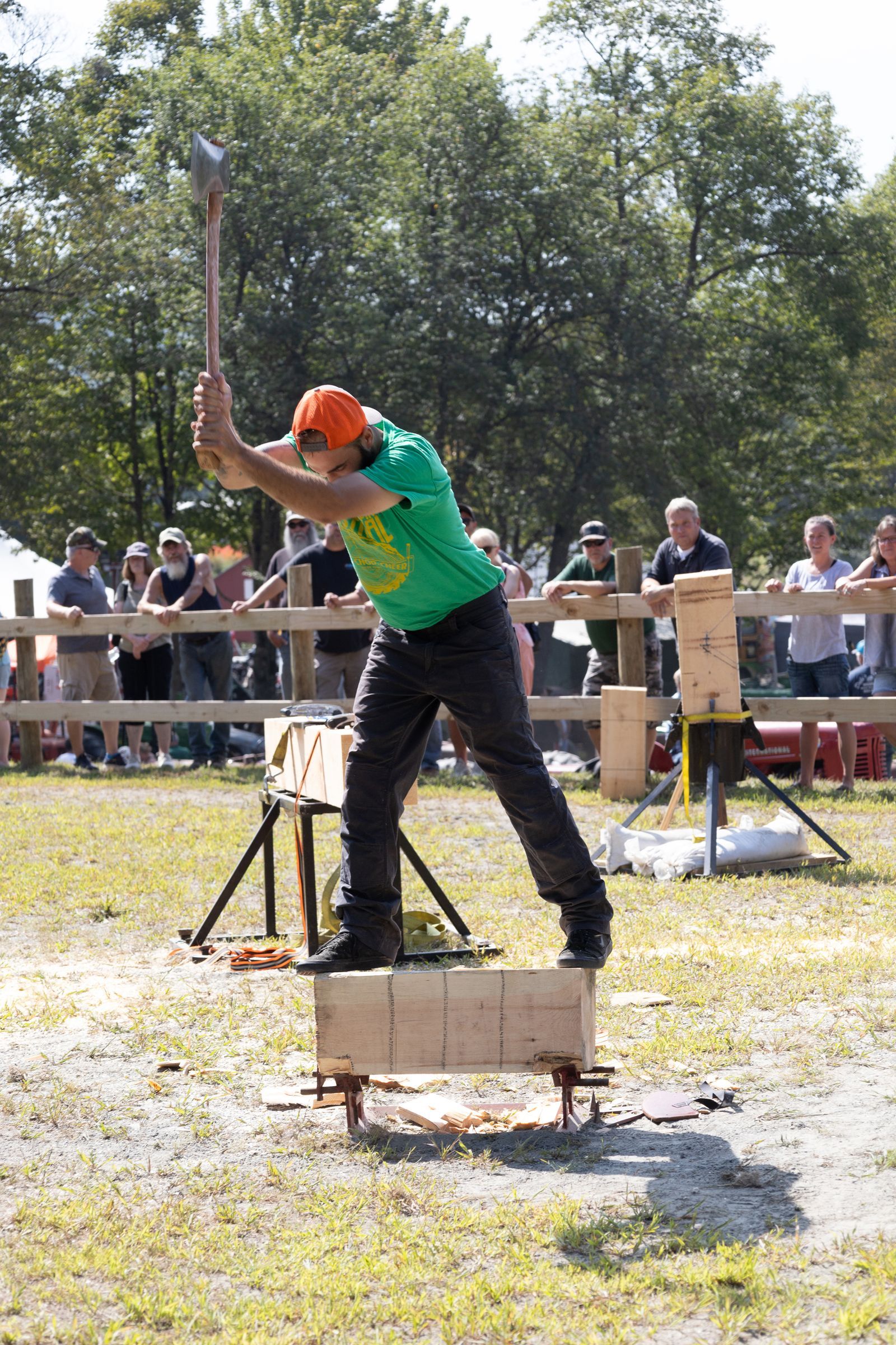 Person in green shirt and orange helmet swings an axe at a target in an outdoor competition
