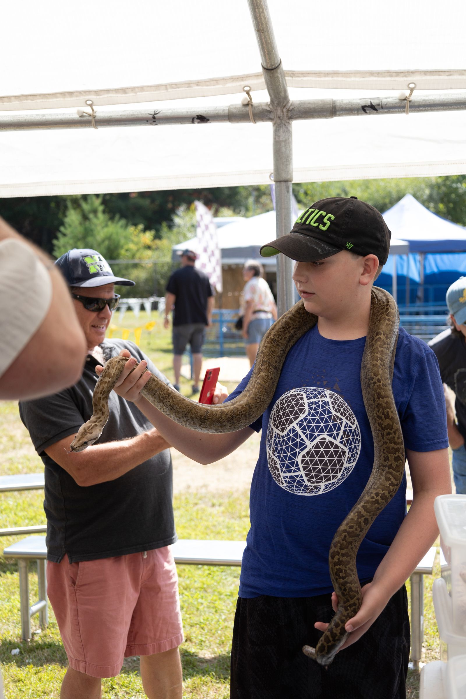 Boy holding a snake at an outdoor event under a tent