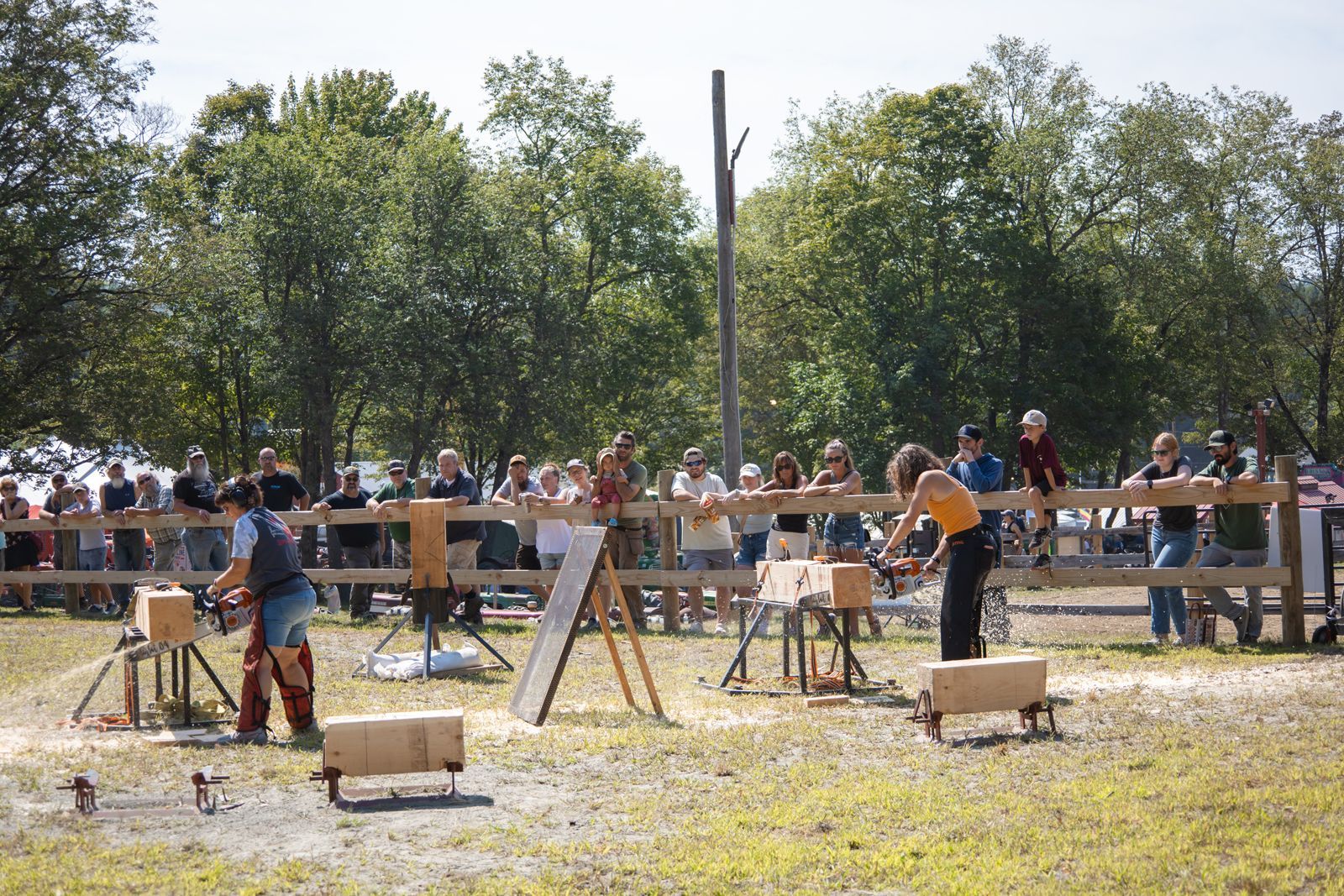 People working at outdoor archery targets in a park, with a crowd and trees in the background