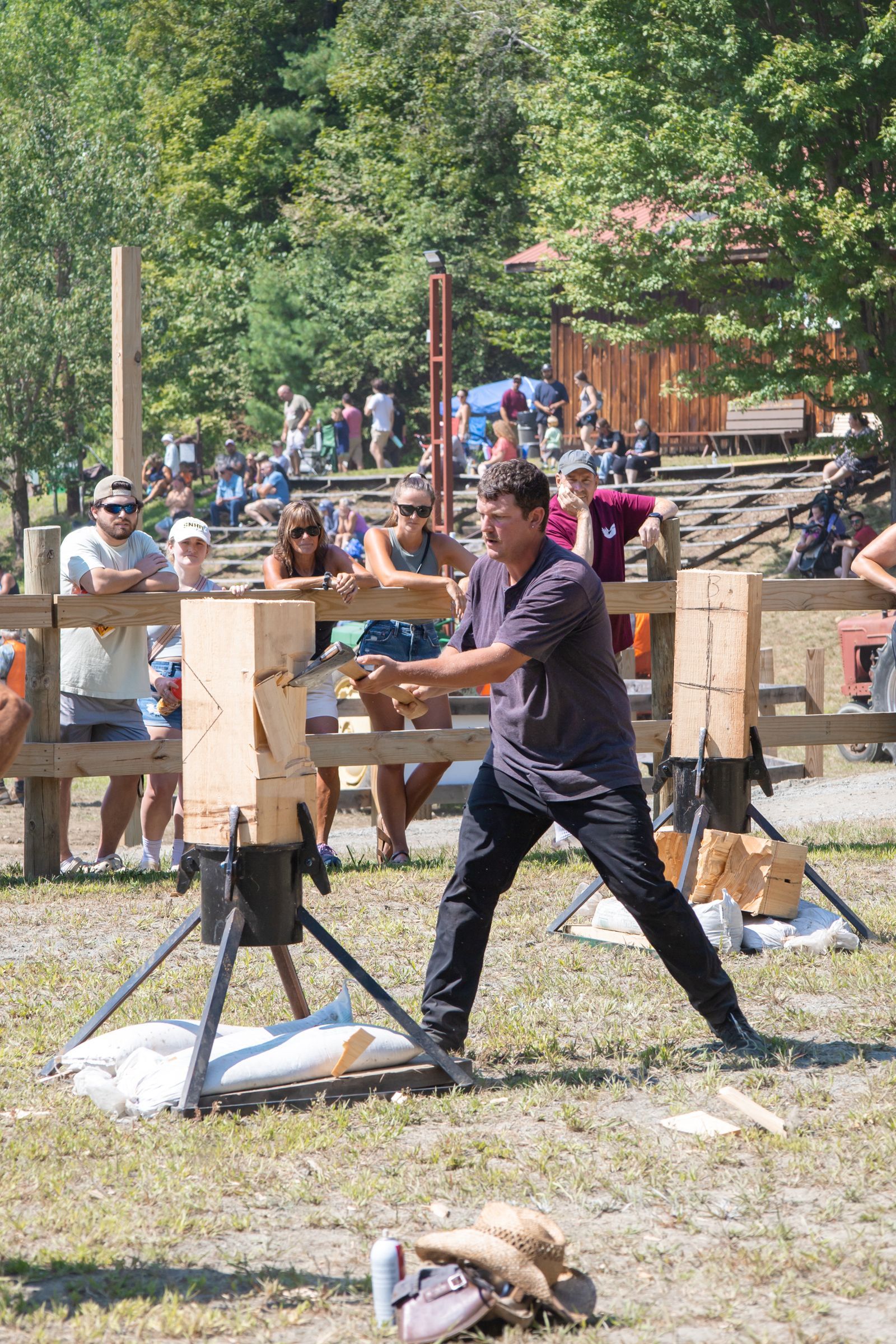Man splitting wood with an axe at an outdoor lumberjack competition, with spectators in the background