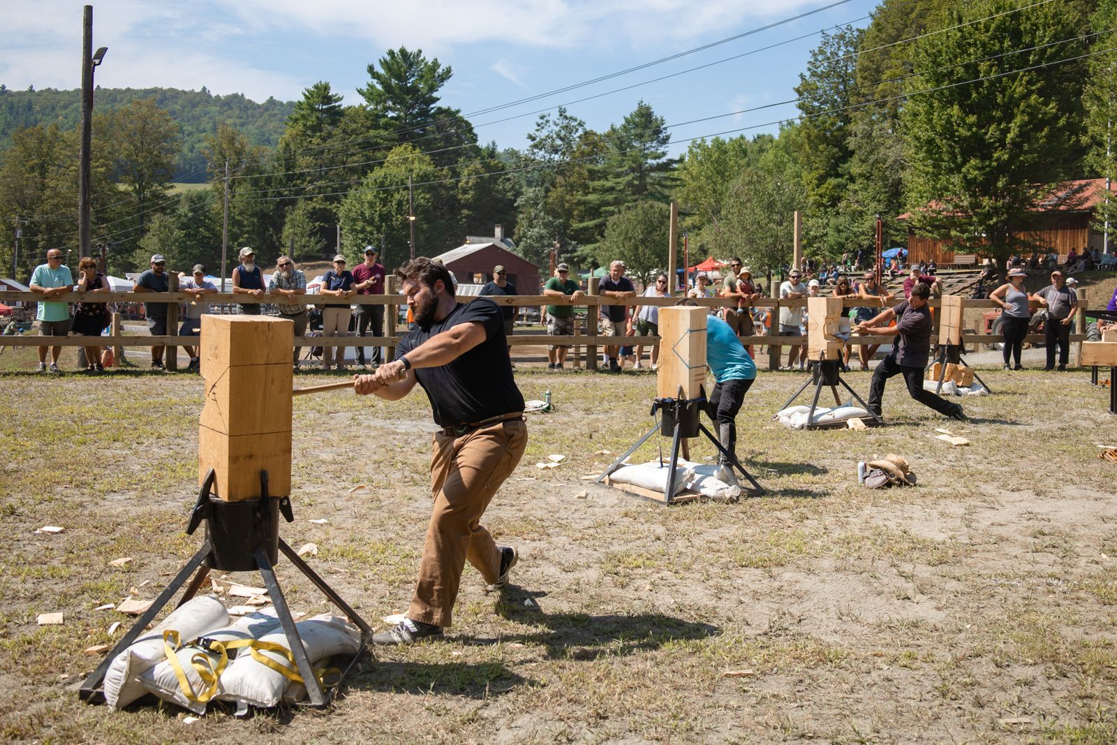 People chopping wood with axes at an outdoor lumberjack competition in a grassy field.