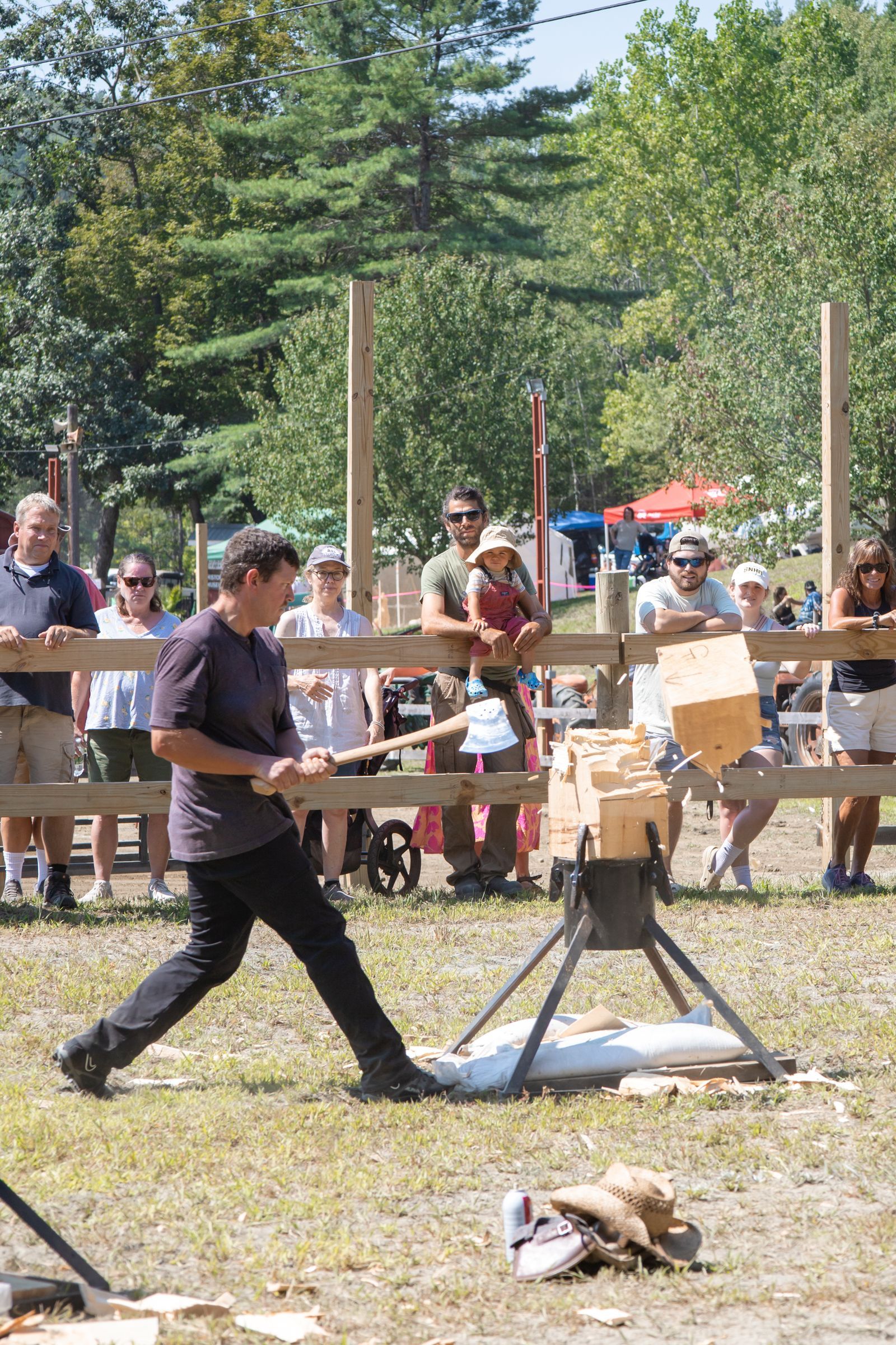 Man swinging a bat at a makeshift outdoor game target with spectators watching behind him