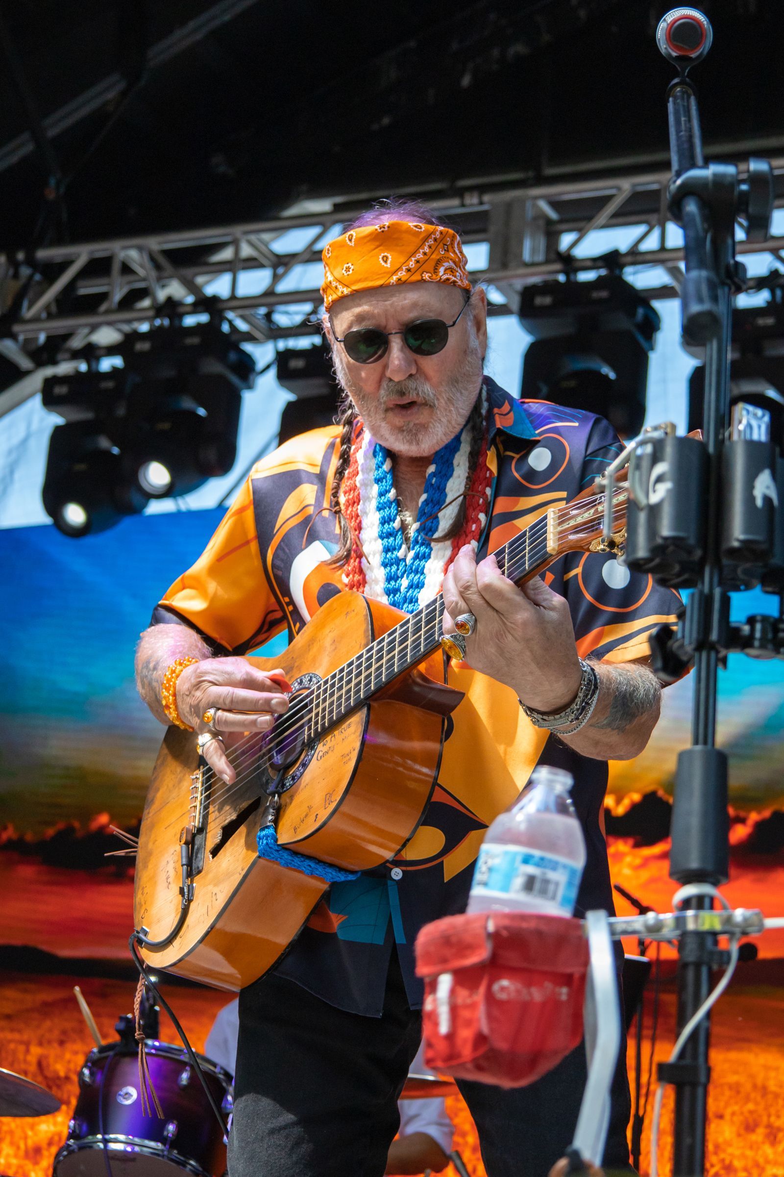 Musician in orange bandana and shirt playing guitar onstage under concert lights