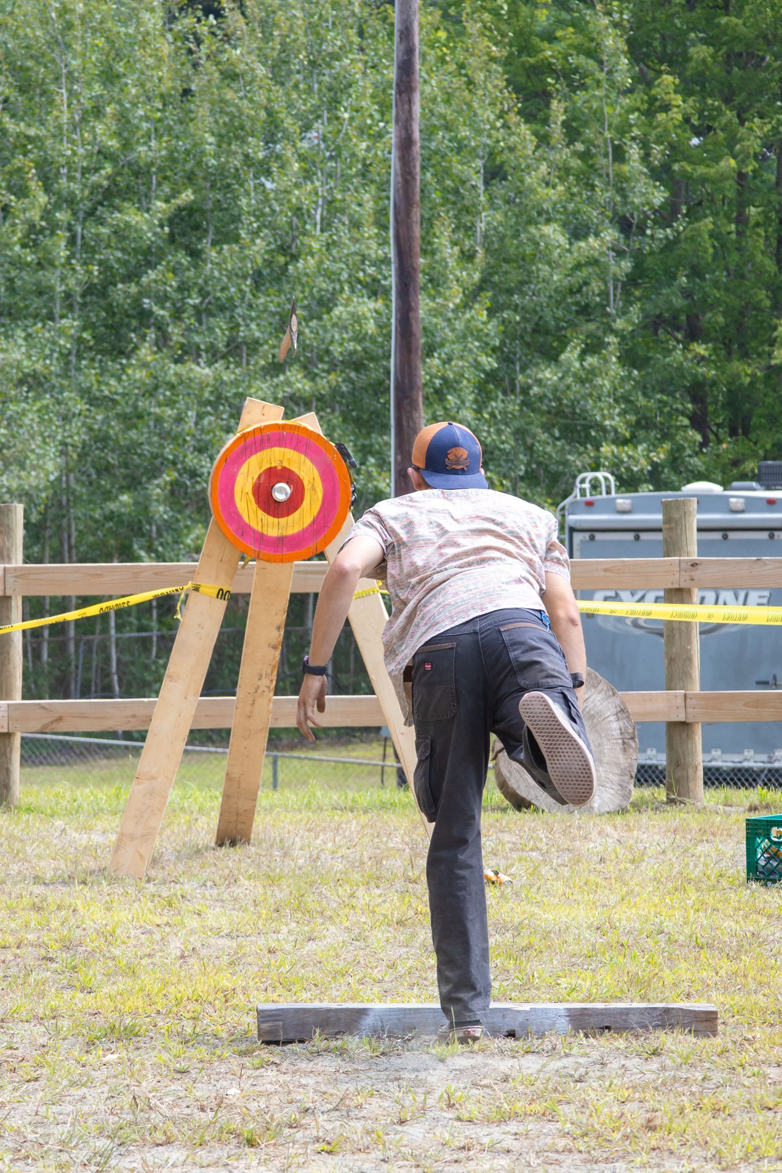 Person throwing a hatchet at a red-and-yellow target outdoors, mid-swing
