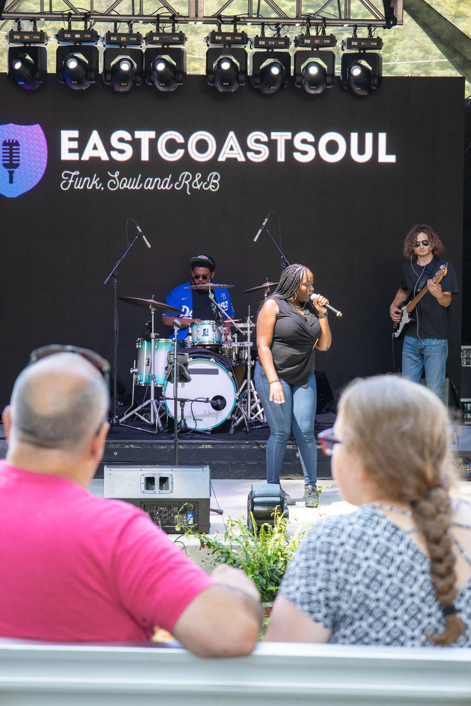 Outdoor live band performance on stage with EastCoastSoul banner, viewed from an audience seating area