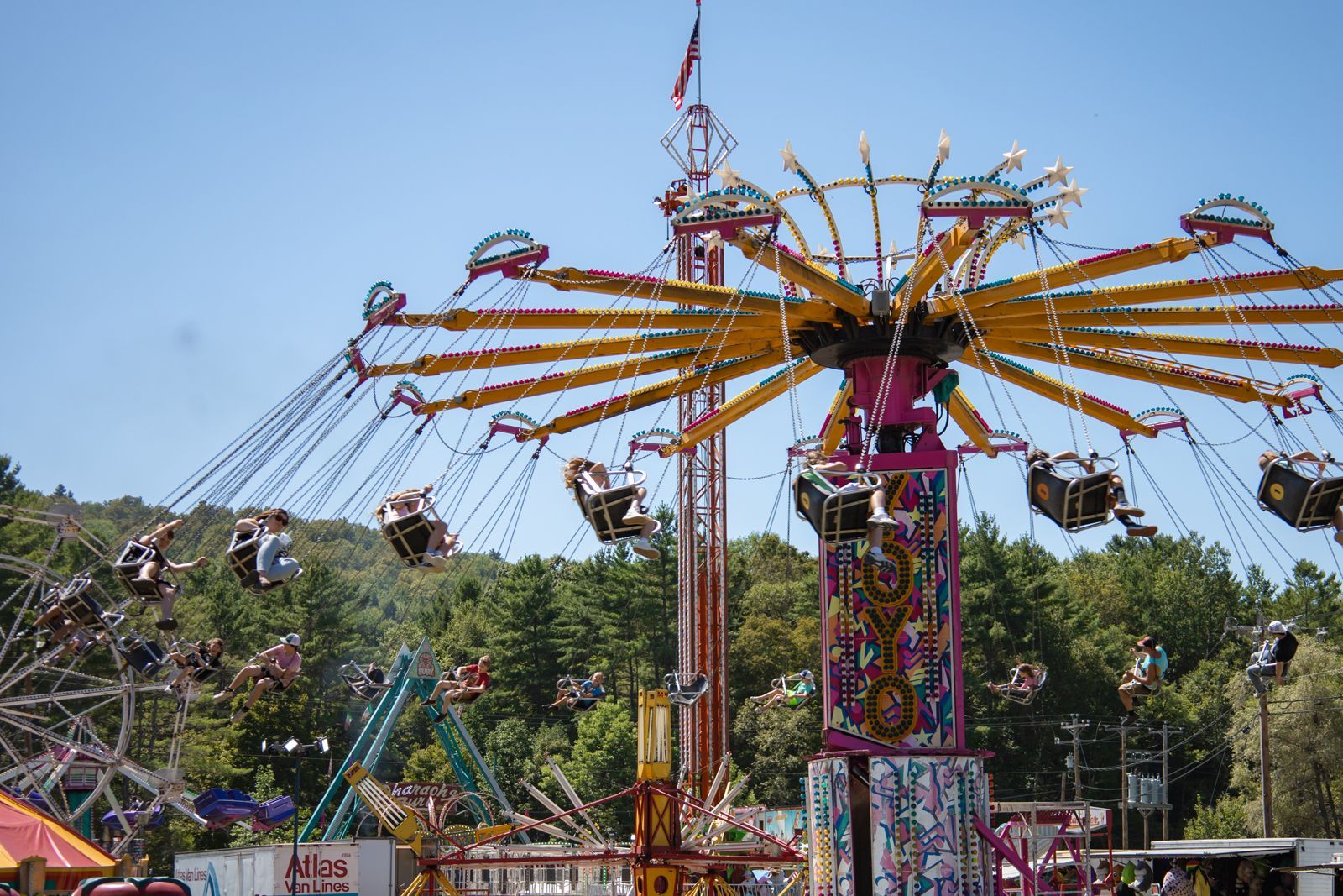 Colorful swing ride spinning at a fair, with yellow arms and seats against a blue sky