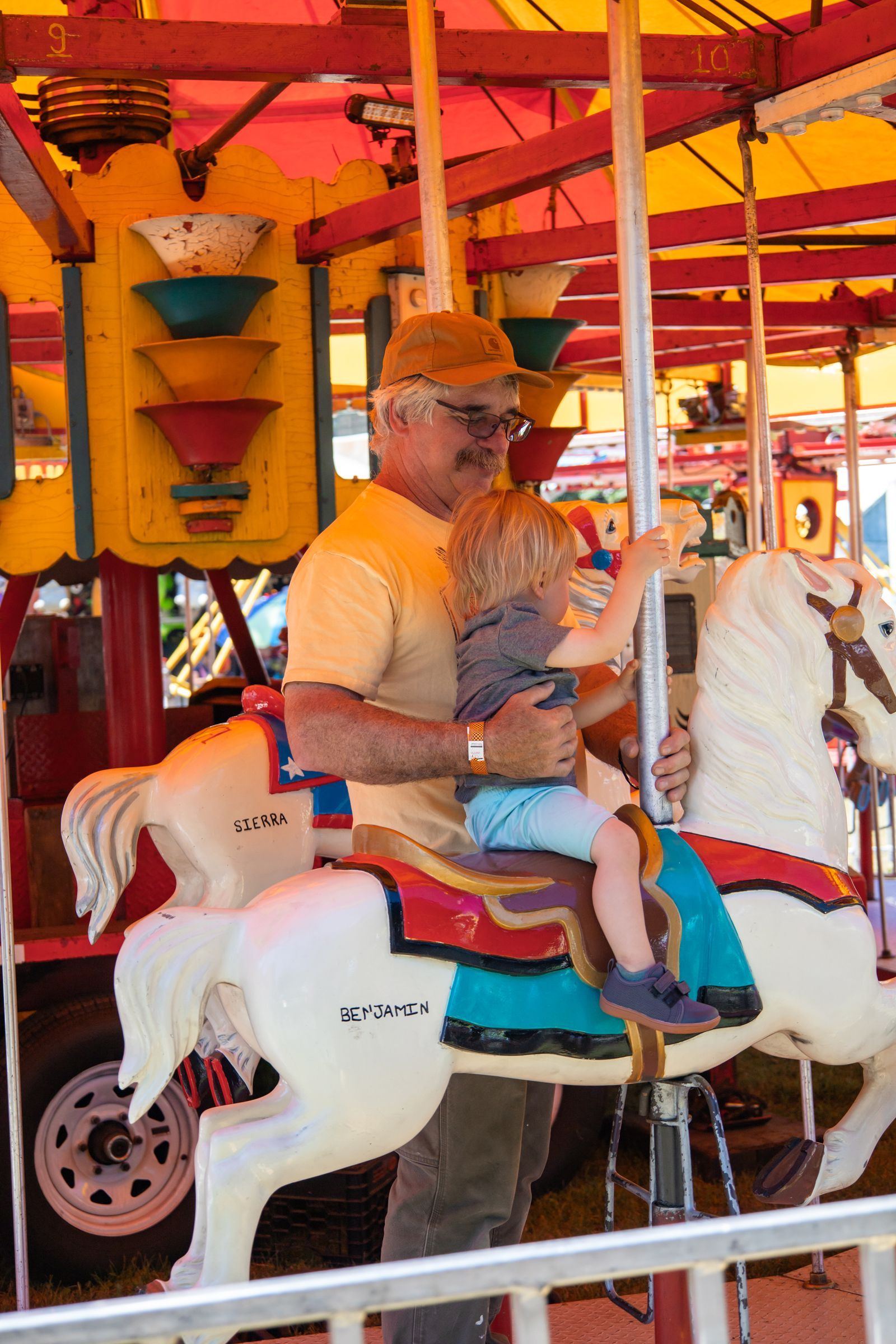 Person riding a white carousel horse under a red-and-yellow canopy at an amusement ride