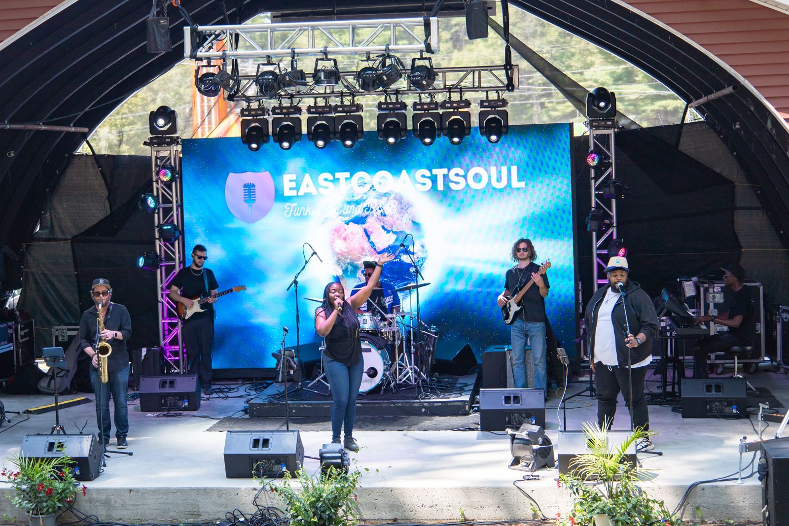 Band performing on an outdoor stage with a large LED screen backdrop and lighting rig