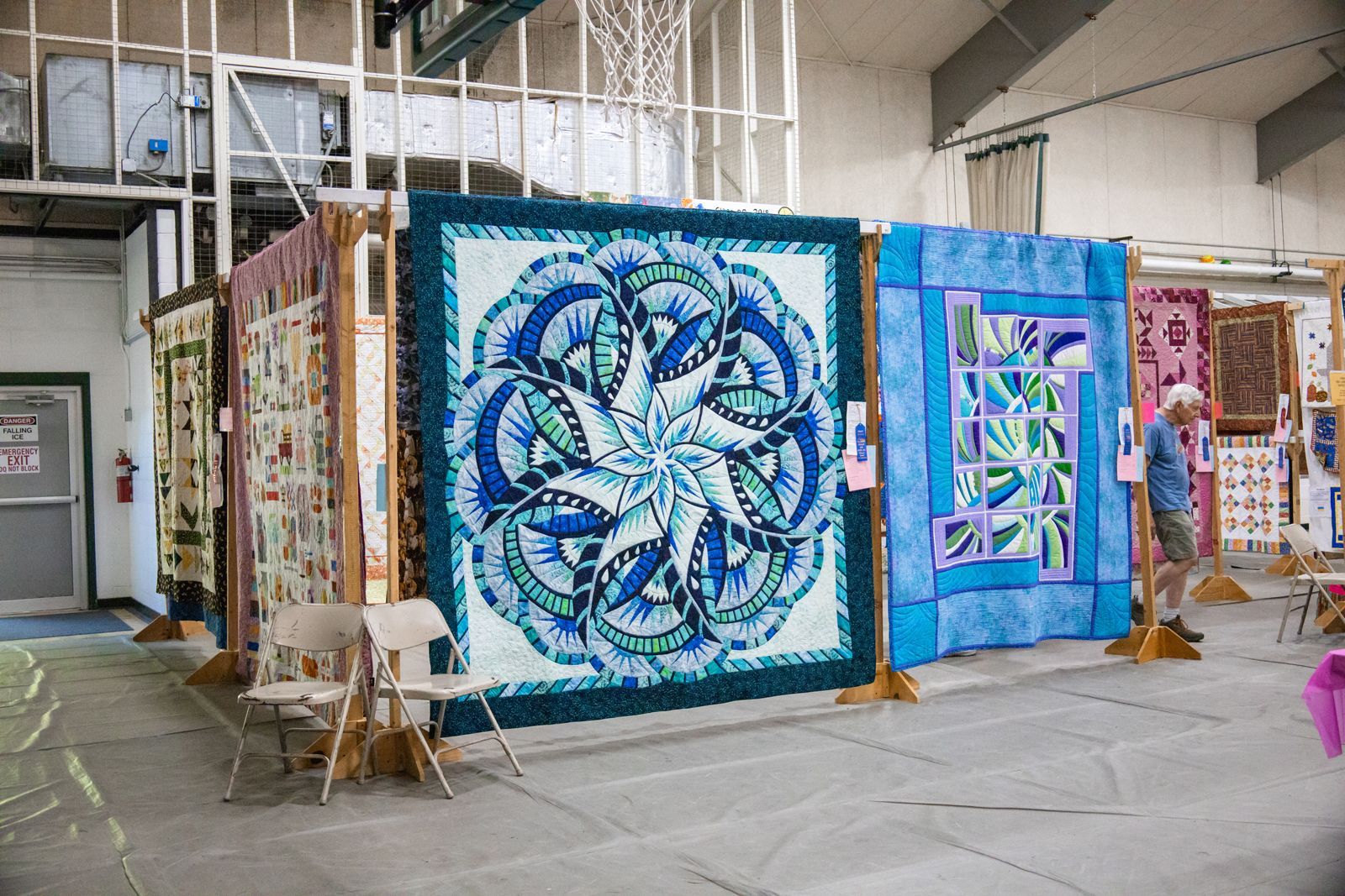 Colorful quilt display in a gallery, with large blue and purple textile panels hanging in a row.