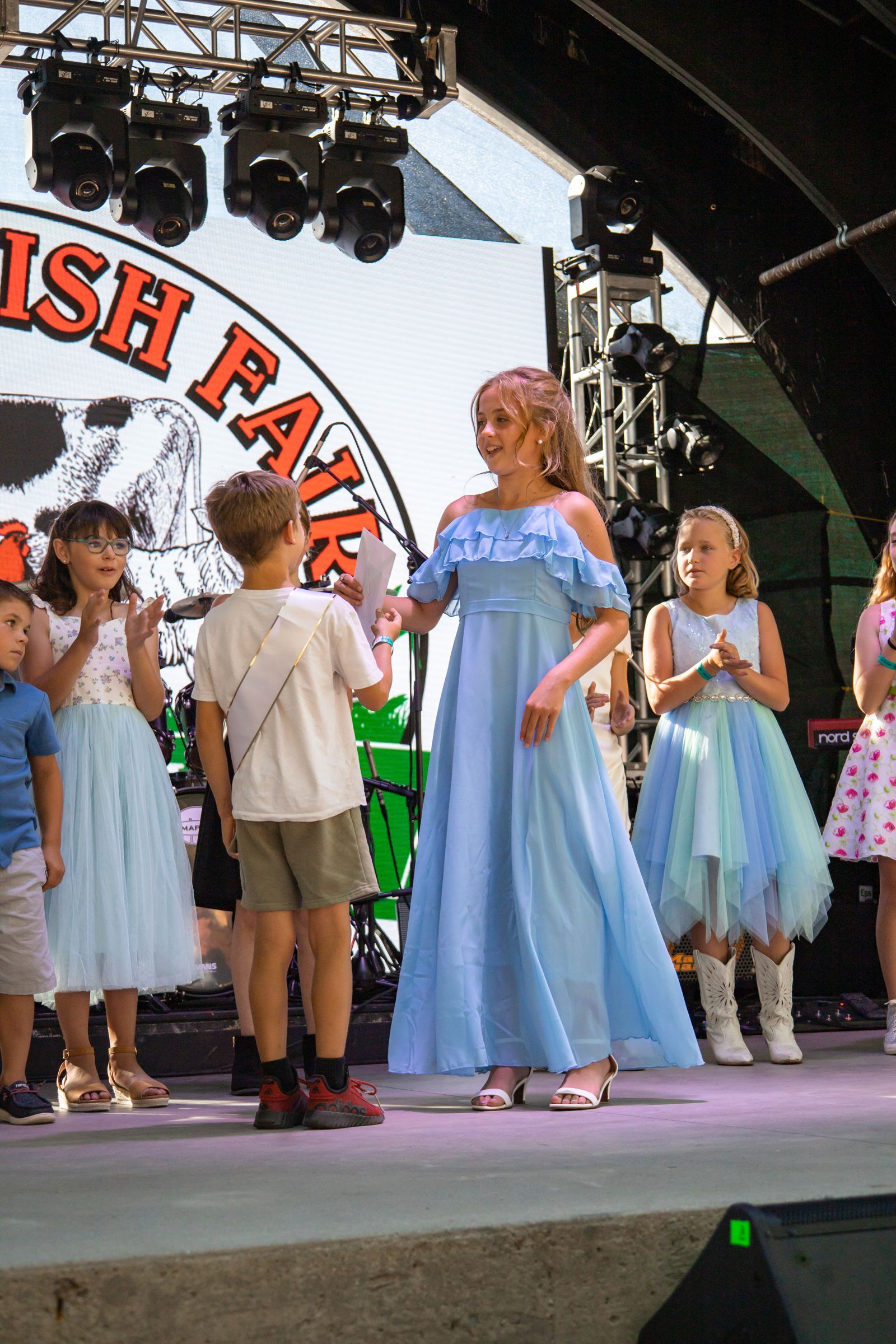 Children and a woman in blue dresses on an outdoor stage at a festival