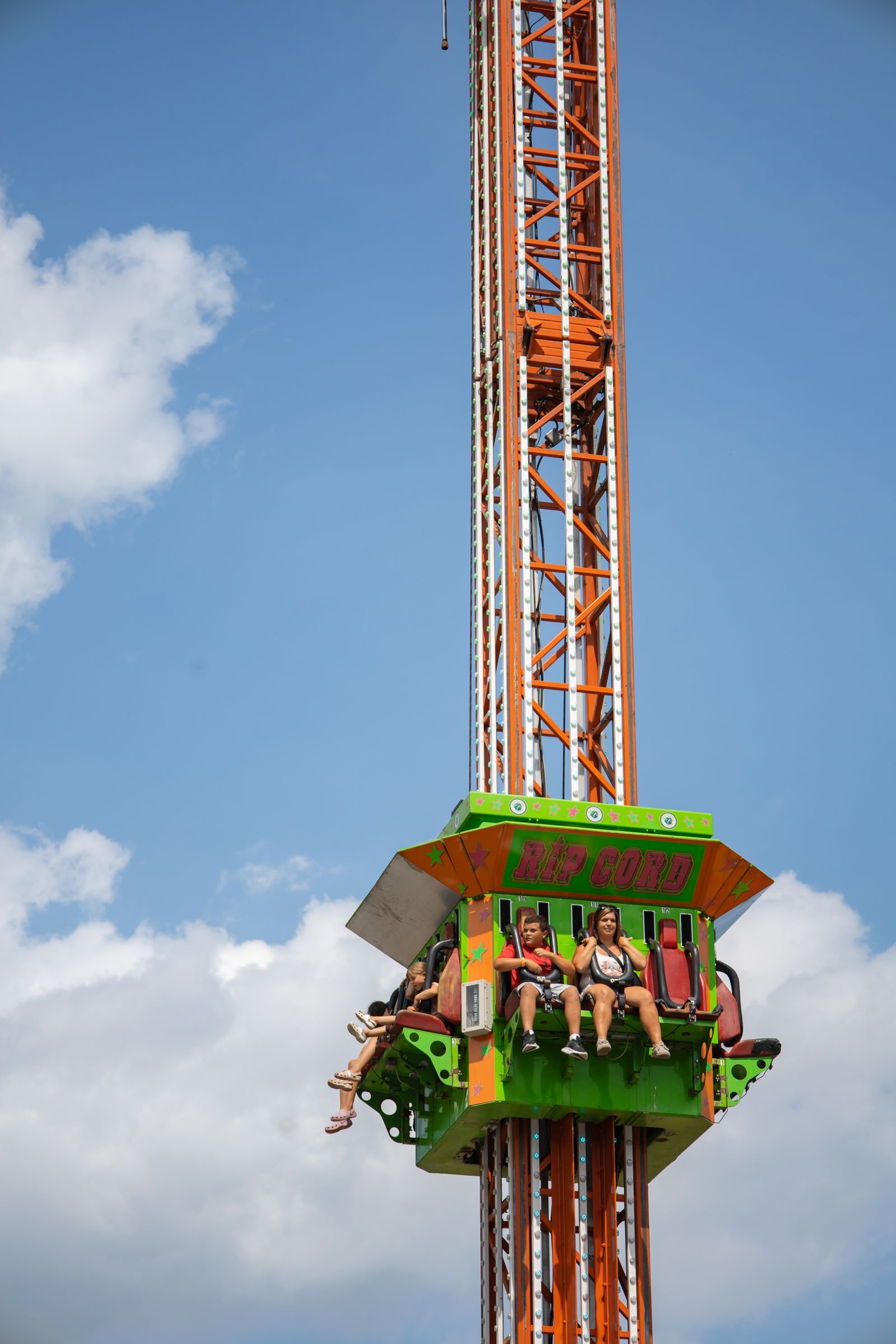 People riding a bright green amusement park drop tower against a blue sky
