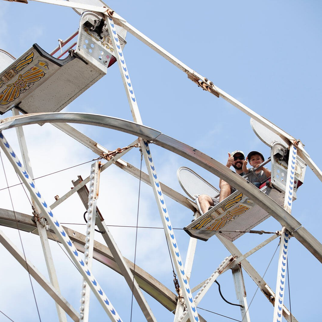 Children riding a white Ferris wheel against a clear blue sky
