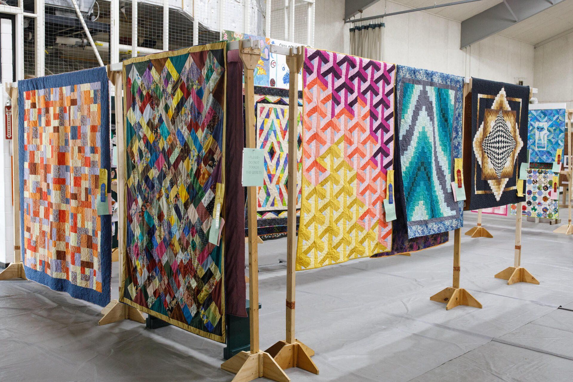 Colorful quilt panels displayed on stands in a covered outdoor exhibit area