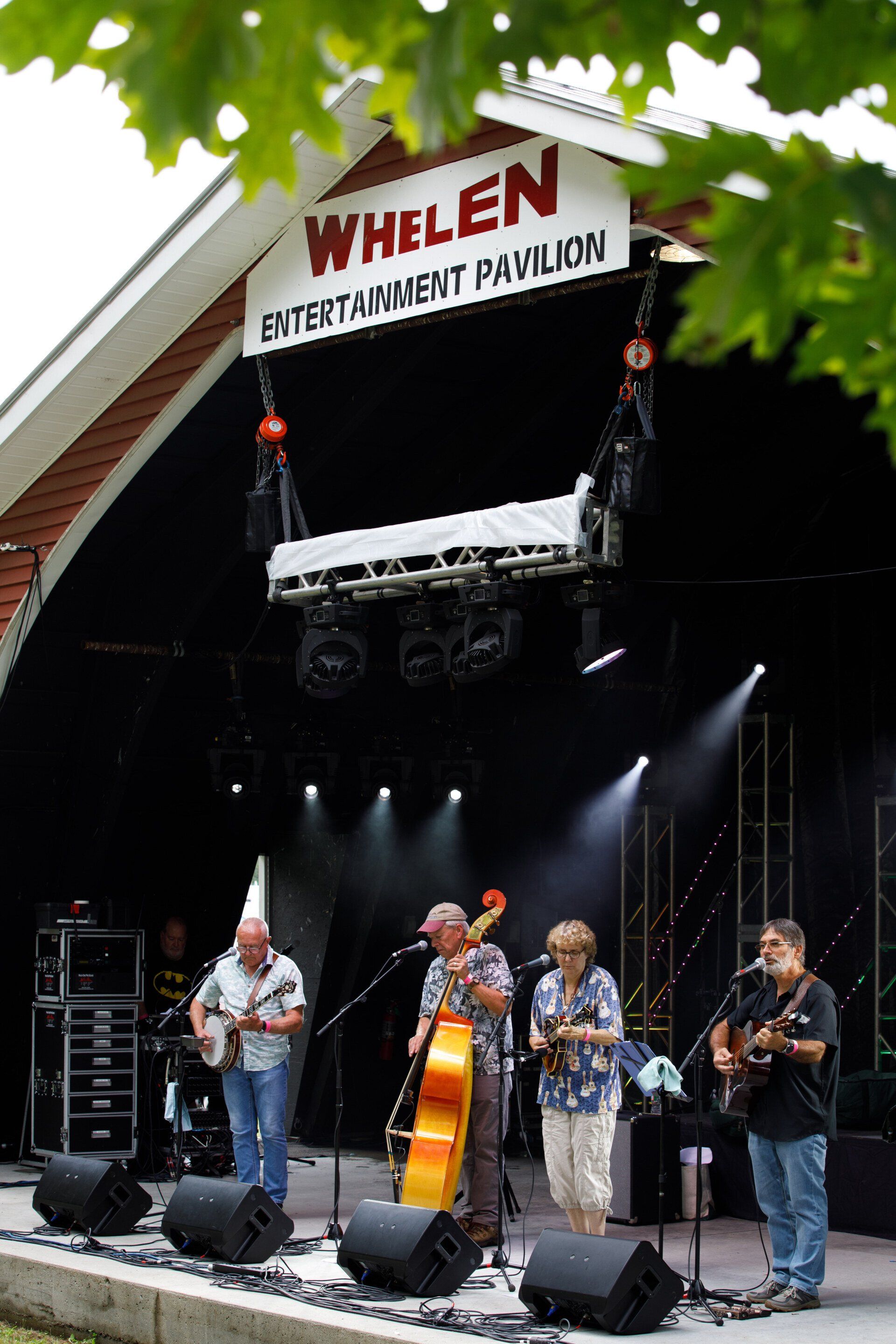 A group of men are playing instruments on a stage under a sign that says whelen entertainment pavilion